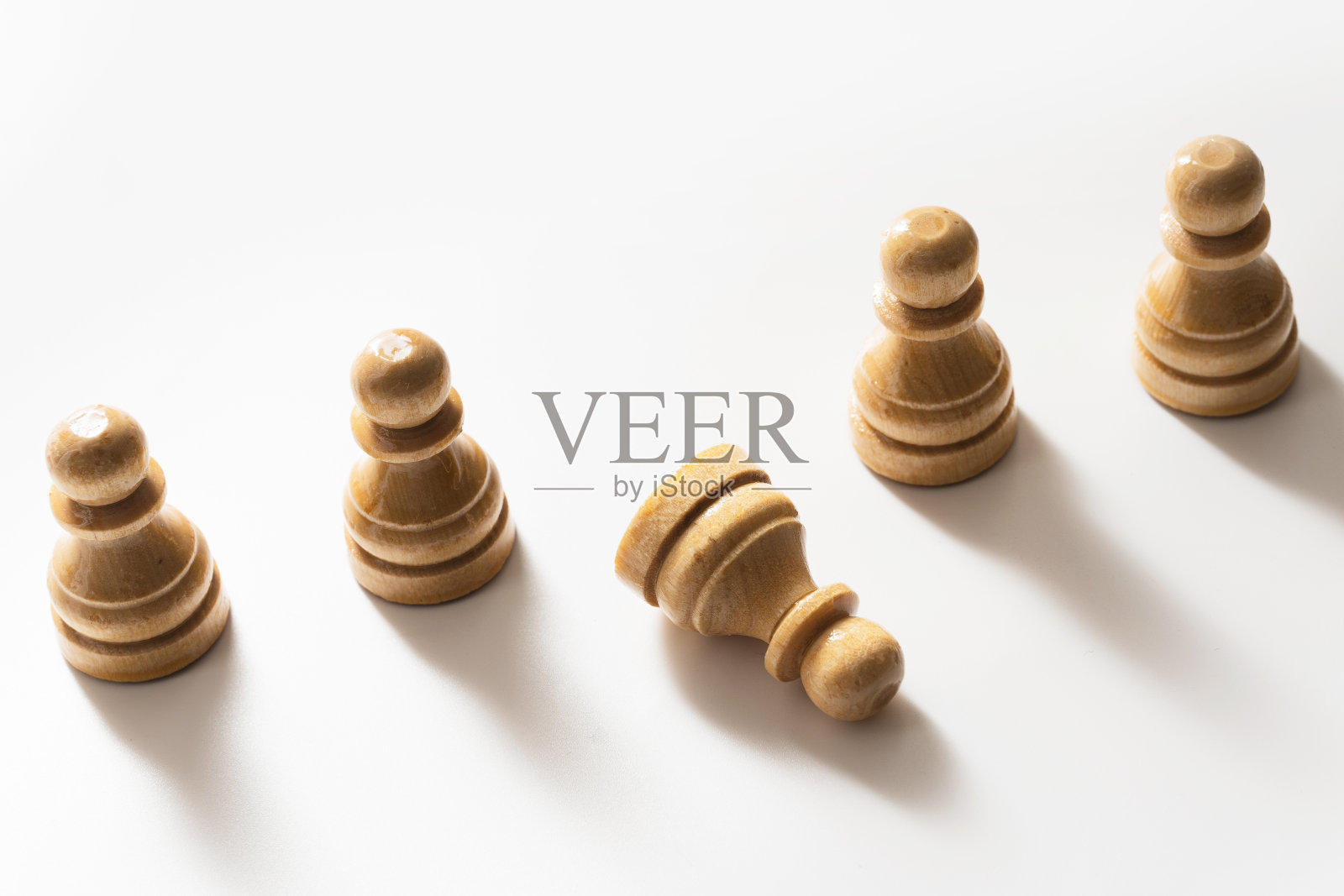 木制棋子站着，一个棋子躺在地上。照片摄影图片