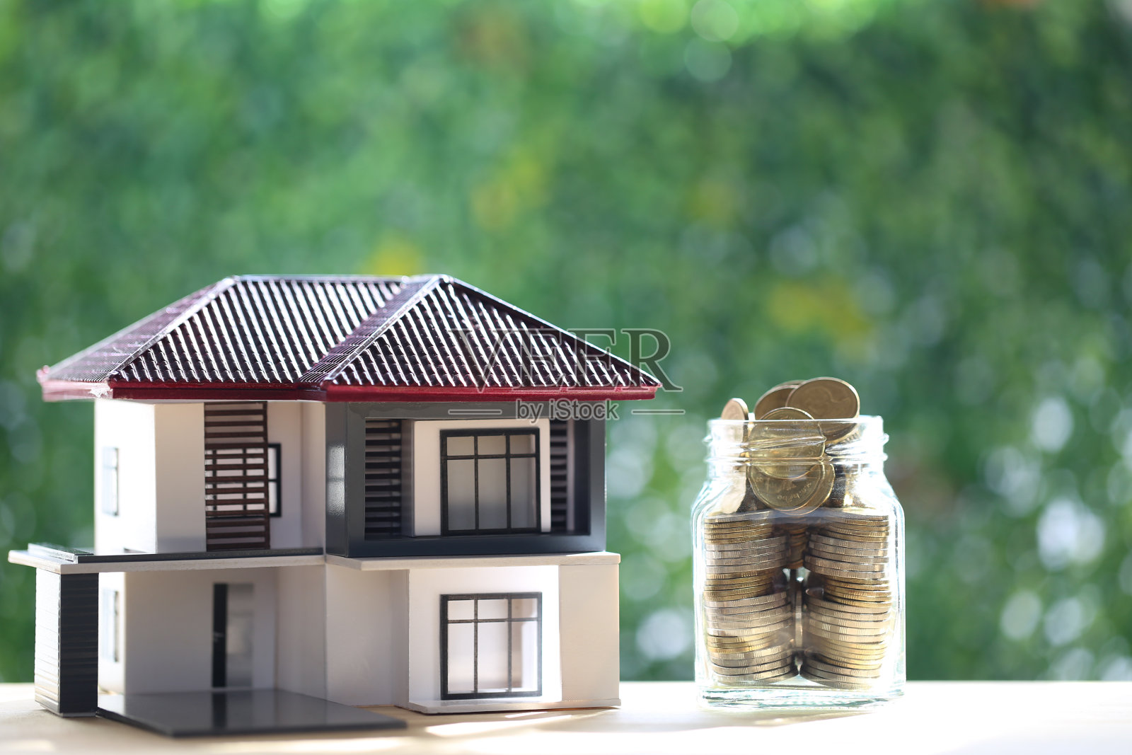 模型房子和叠硬币在玻璃瓶上的自然绿色背景，商业投资和房地产概念照片摄影图片