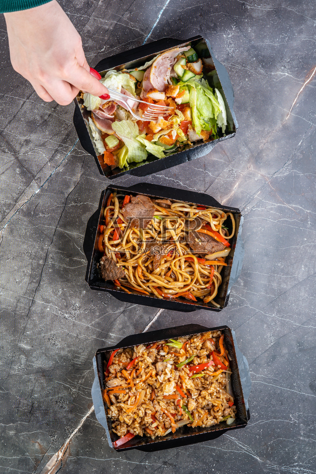 女性手拿食物俯视图。牛肉乌冬面，沙拉和蒂里亚烧酱米饭。盒装韩国食品。食品容器的盒子照片摄影图片