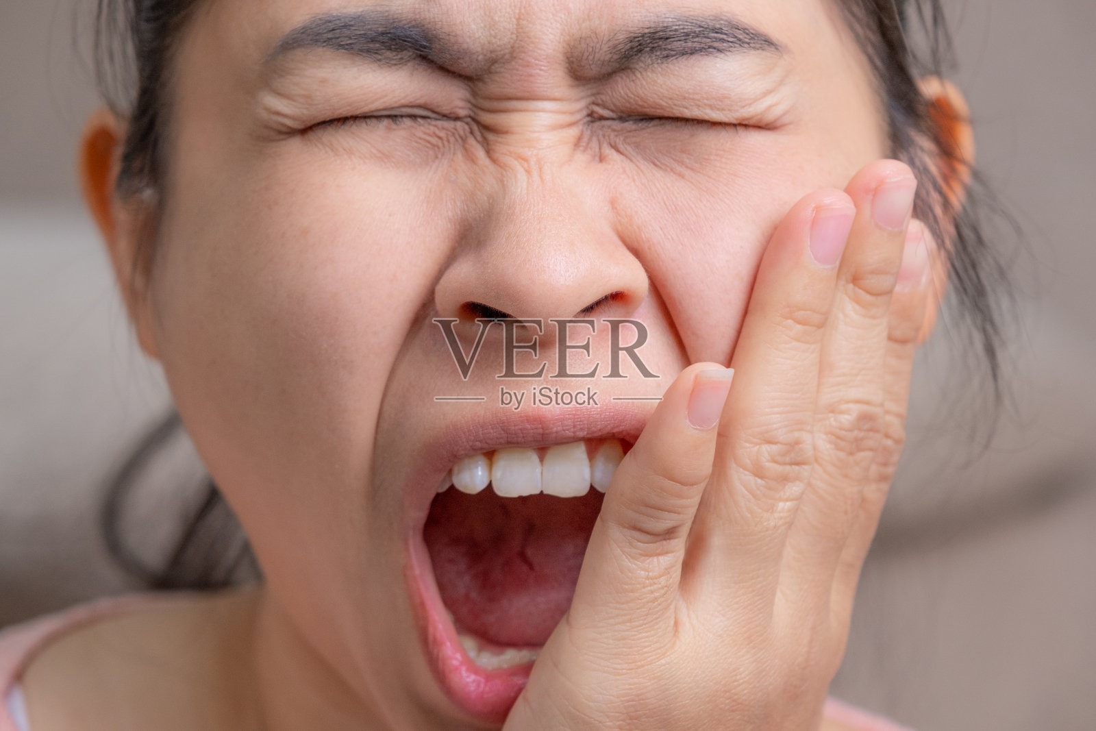 亚洲女子用手托着他的脸颊，患有牙痛、蛀牙、牙齿敏感、蛀牙。健康和牙科保健的概念。照片摄影图片