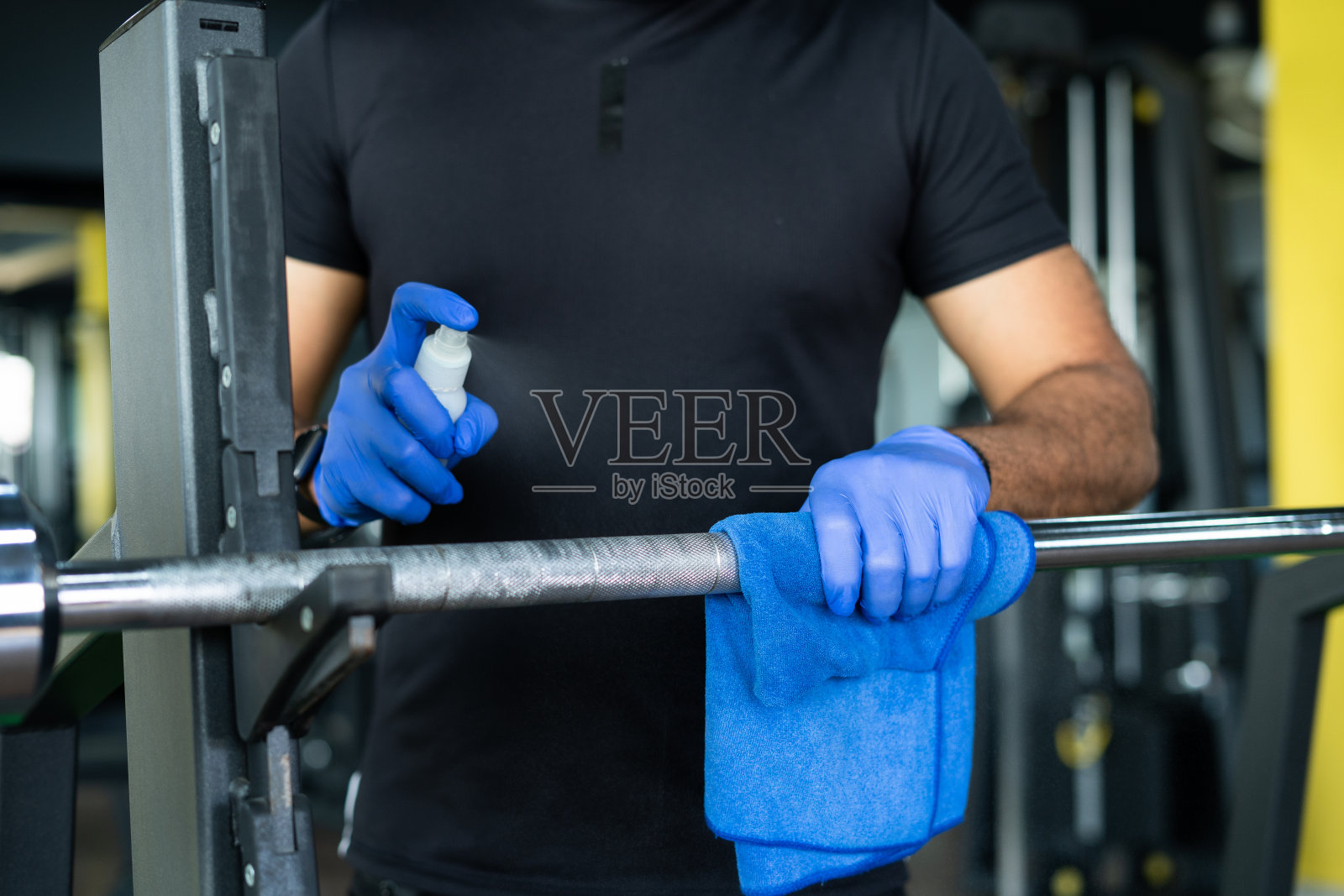 近距离拍摄双手用手套消毒或擦汗的重量照明杆或健身器材由于冠状病毒- COVID-19消毒的概念，防止病毒感染的健身照片摄影图片