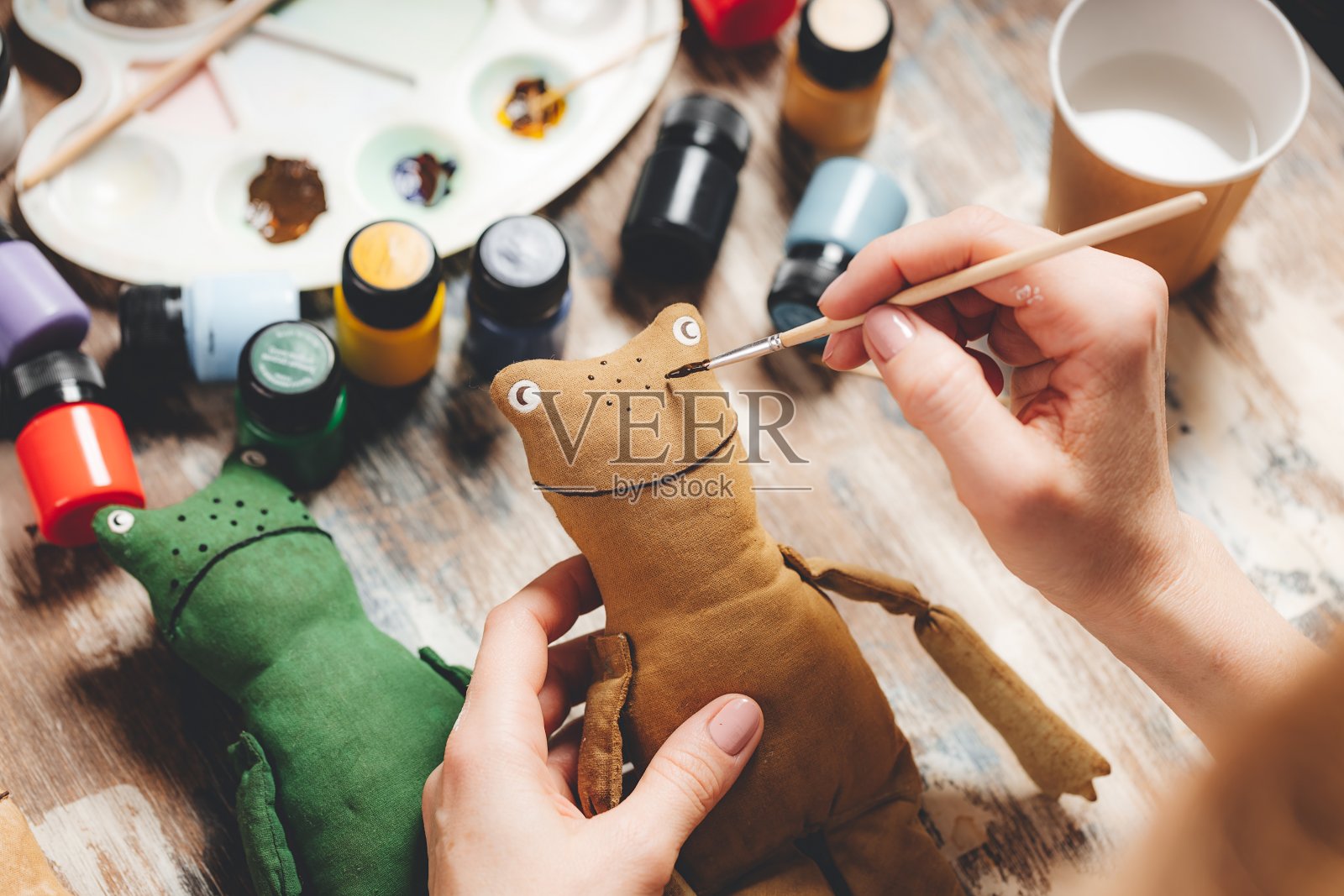 手工制作的软娃娃青蛙。DIY制作的礼物。人类手握青蛙软玩具。刺绣配件在灰色的背景。手工制作的装饰房子。制作老式软玩具的过程。家庭作坊。照片摄影图片