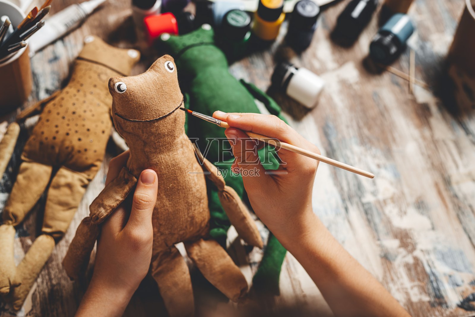 手工制作的软娃娃青蛙。DIY制作的礼物。人类手握青蛙软玩具。刺绣配件在灰色的背景。手工制作的装饰房子。制作一个老式的软玩具的过程。家庭作坊。特写镜头照片摄影图片