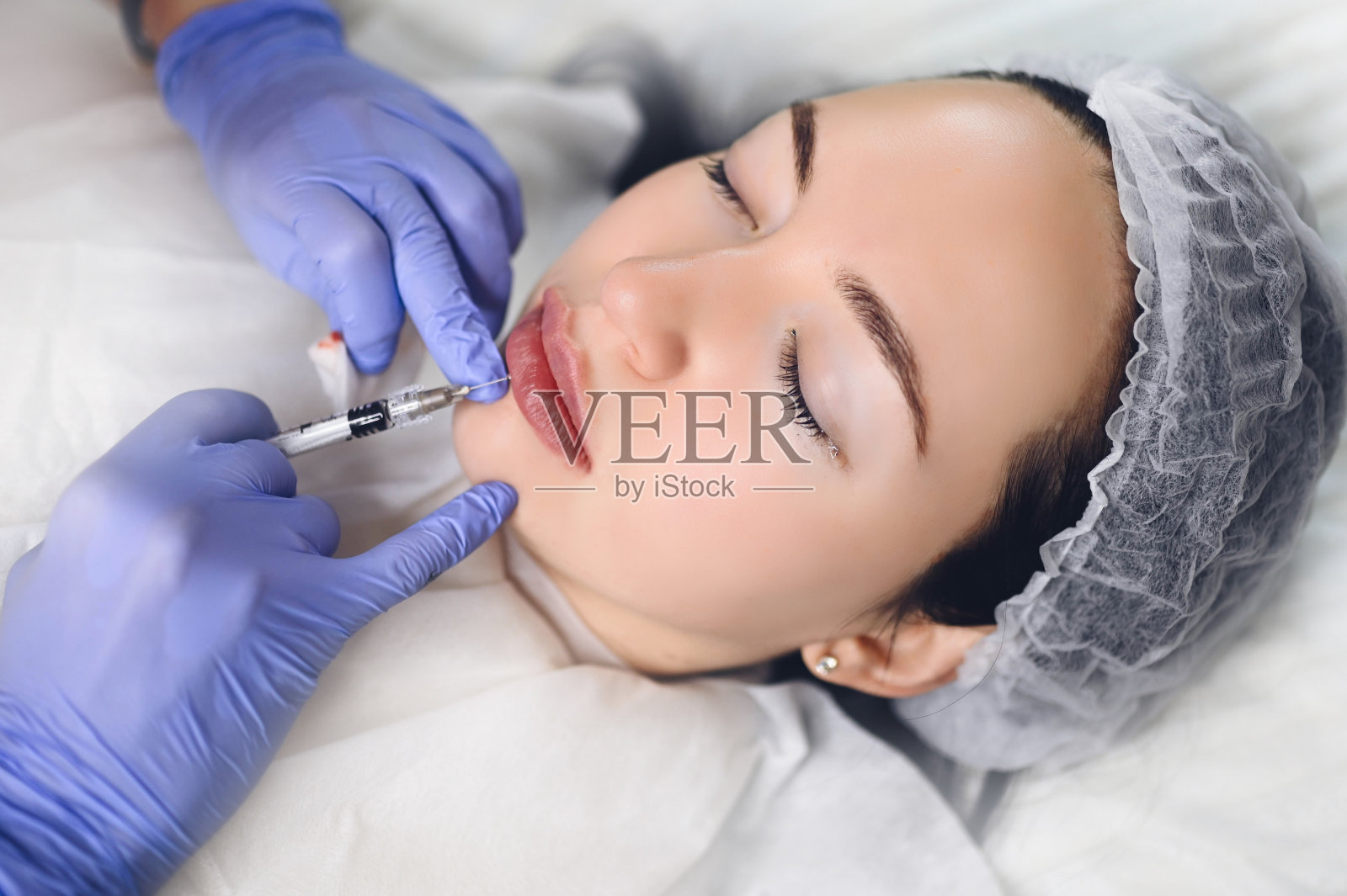 美容院用透明质酸做丰唇手术。美容师用针刺穿嘴唇。年轻女子正在做皮下注射以增加嘴唇形状照片摄影图片