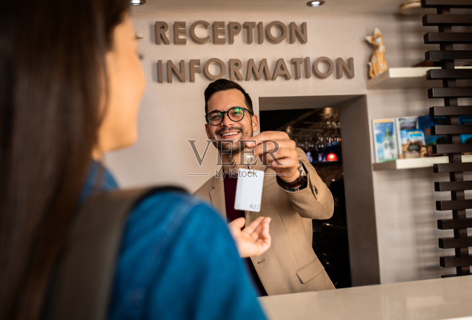 微笑的前台接待员把房间钥匙交给客人。照片摄影图片