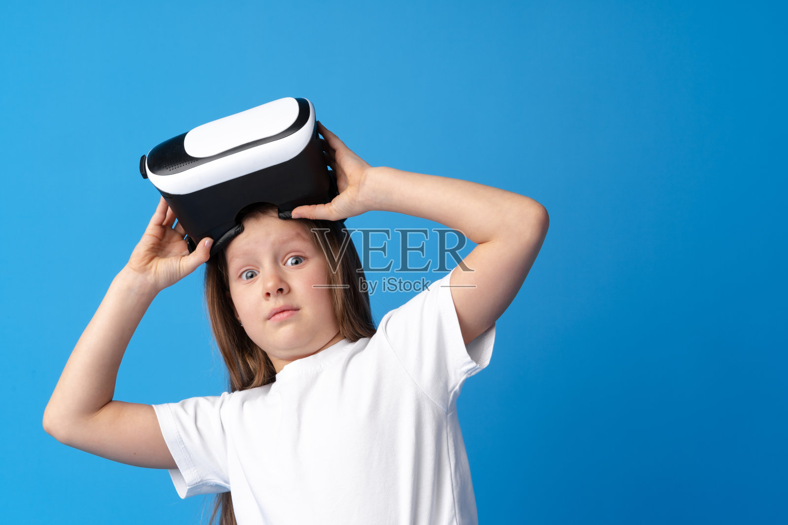 戴着蓝色背景的虚拟现实眼镜的女孩。照片摄影图片