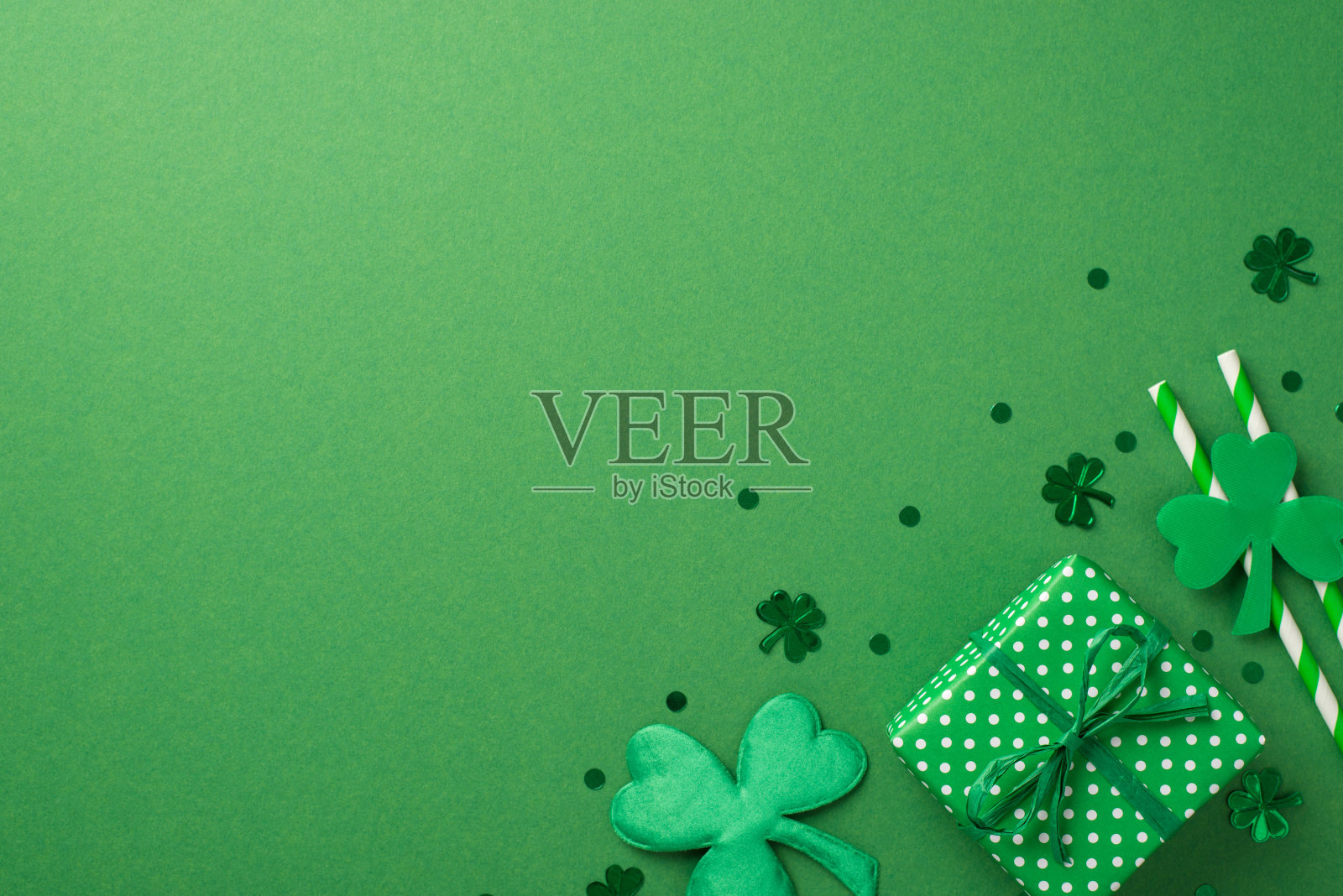 俯视图照片的礼盒与绿色丝带，两条纹吸管饮料和许多不同大小的纸屑三叶草形状和点在绿色孤立的背景copyspace照片摄影图片
