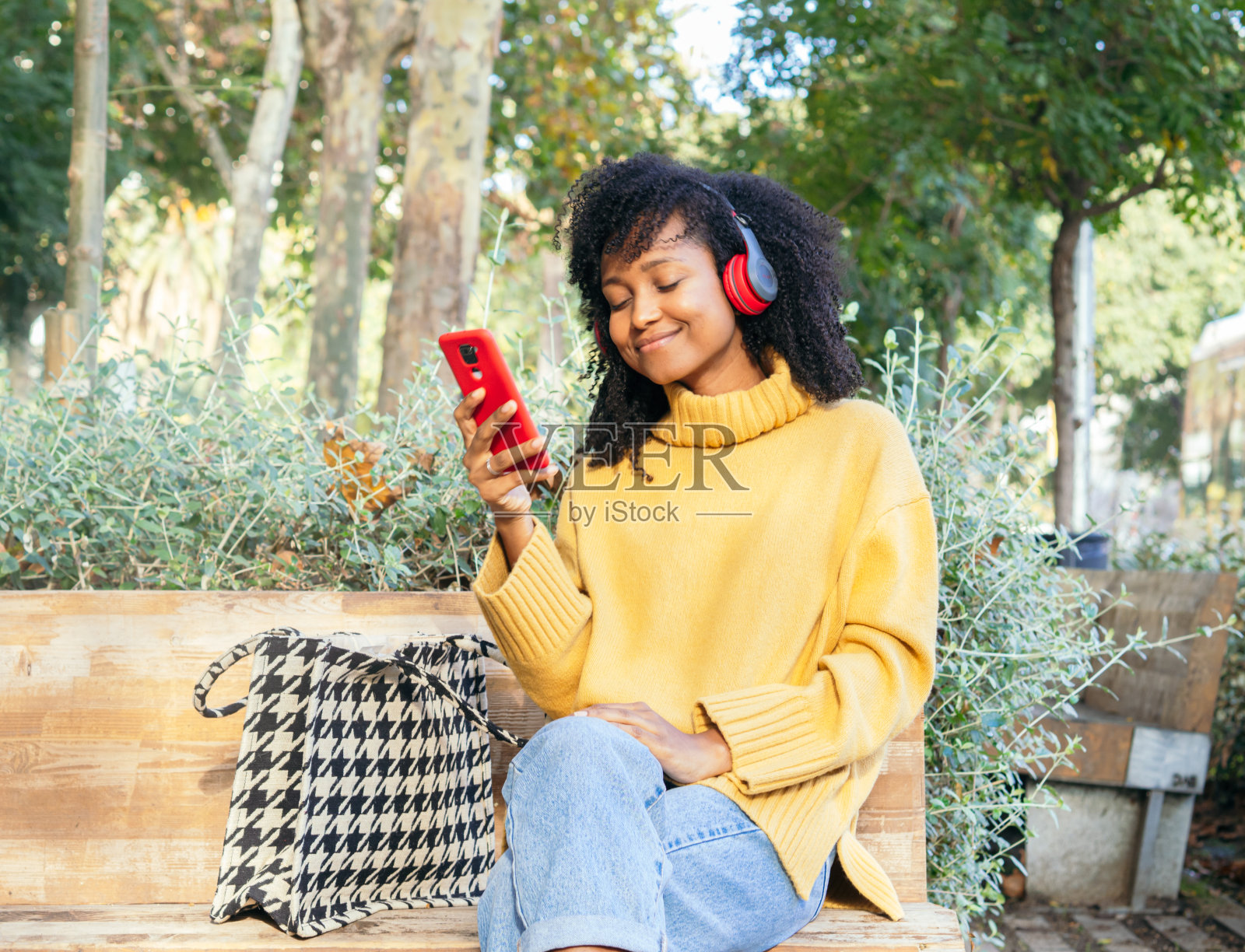 一个乐观的巴西年轻女子戴着耳机坐在长椅上用智能手机聊天。照片摄影图片