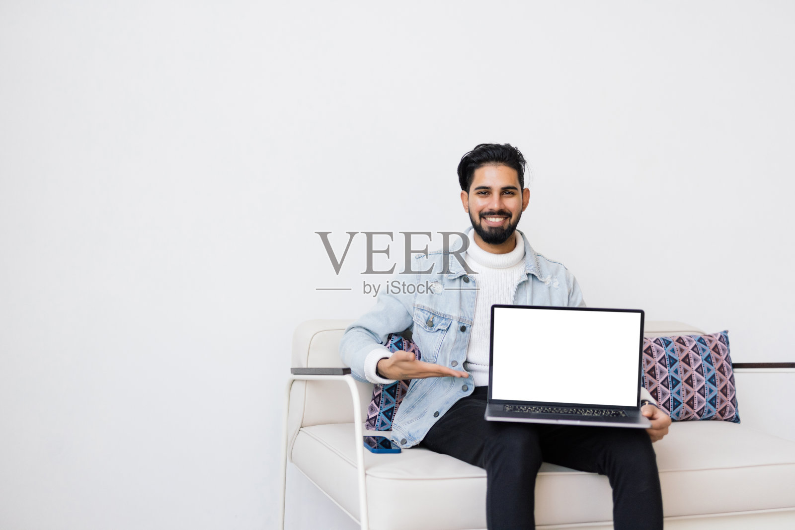 一个年轻人舒舒服服地躺在沙发上，一边使用空白屏幕的笔记本电脑。照片摄影图片