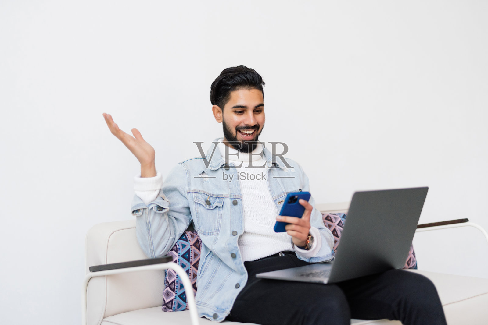 困惑的印度商人在打电话，拿着手机做手势，看着笔记本电脑照片摄影图片