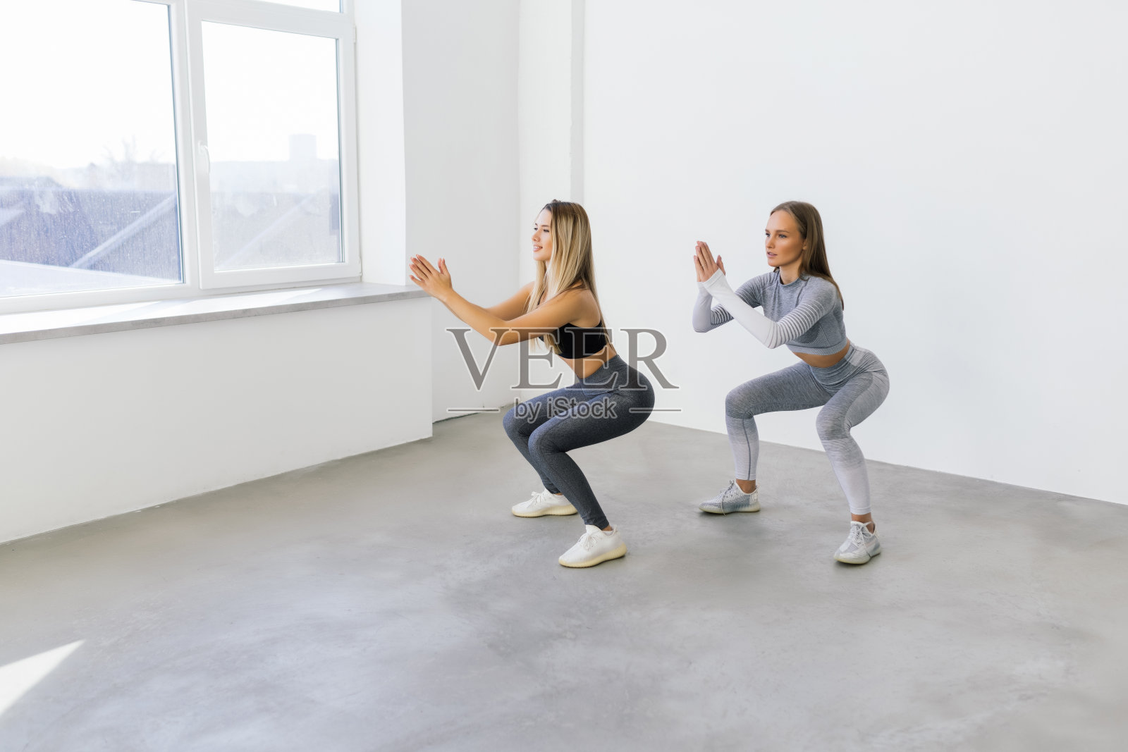 两个健康的女人做深蹲在家里，女性锻炼运动和健身。照片摄影图片