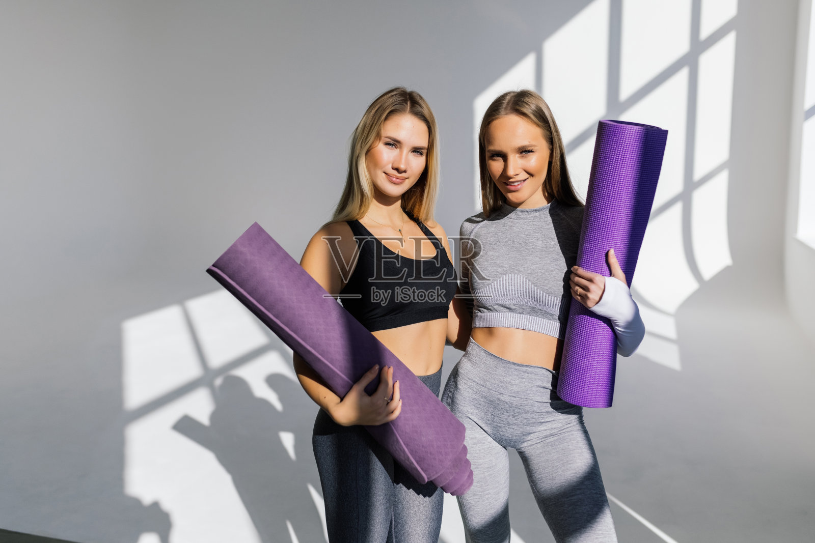 两个女运动员朋友穿着运动服，在运动课上垫着瑜伽垫。健康的生活方式照片摄影图片