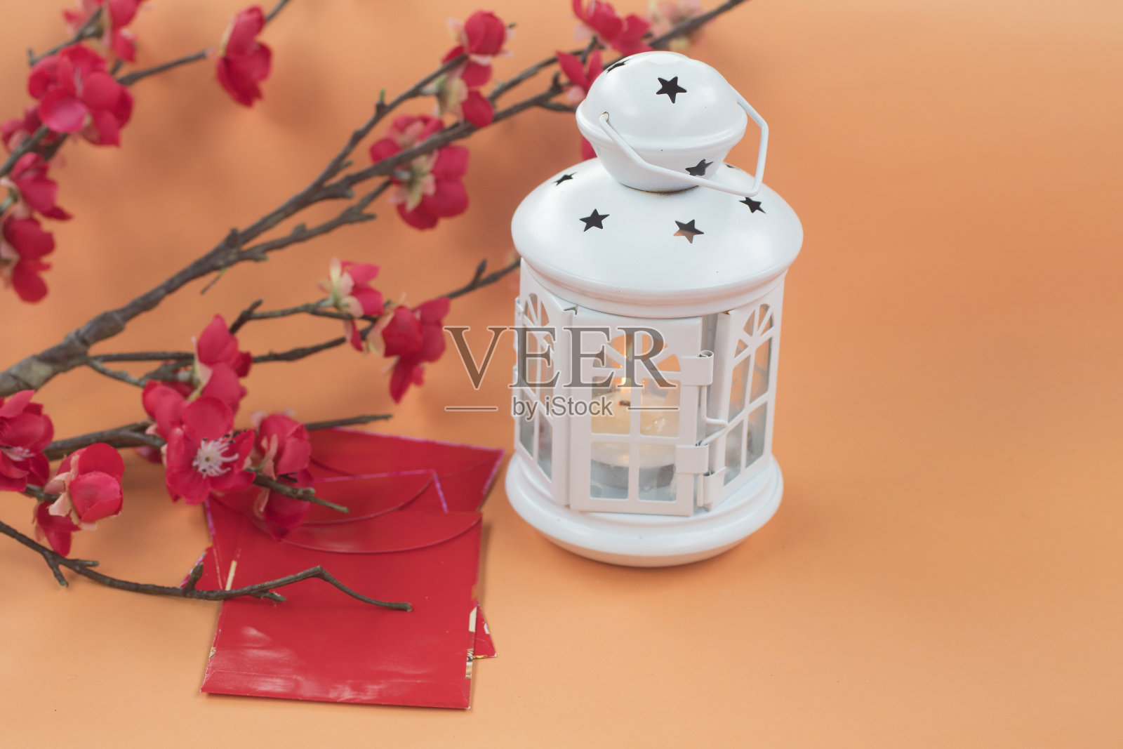 白色灯笼，里面点着蜡烛，红色的信封和树枝装饰在软橙色的背景上。照片摄影图片