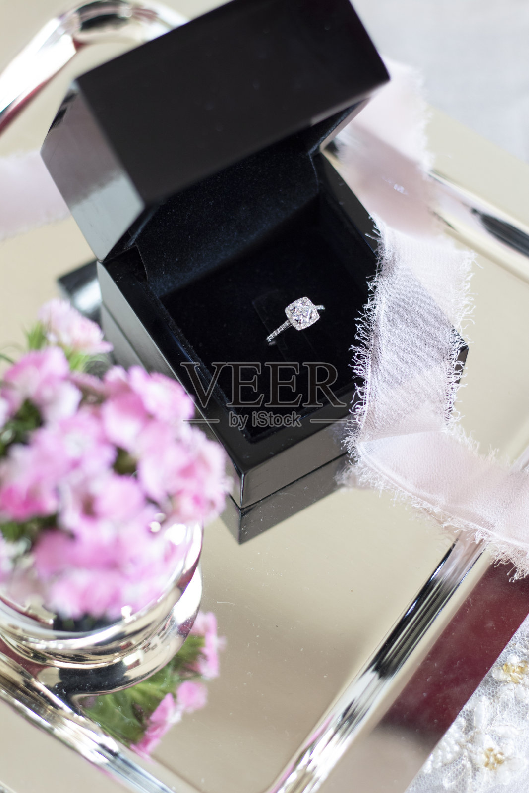 豪华钻石订婚接龙戒指在黑色礼品盒与粉红色的花在银托盘照片摄影图片