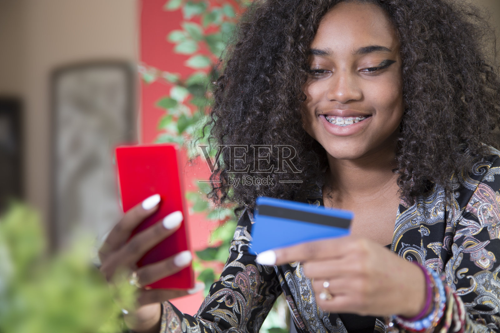 可爱的非裔美国青少年在网上购物。她坐在厨房吧台旁。笔记本电脑、智能手机和信用卡。照片摄影图片