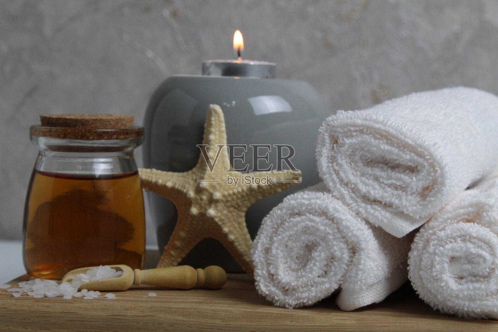 水疗放松按摩居家身体护理。白色毛巾，油香按摩香薰蜡烛，星海躺在一个灰色背景侧视图木制托盘上照片摄影图片