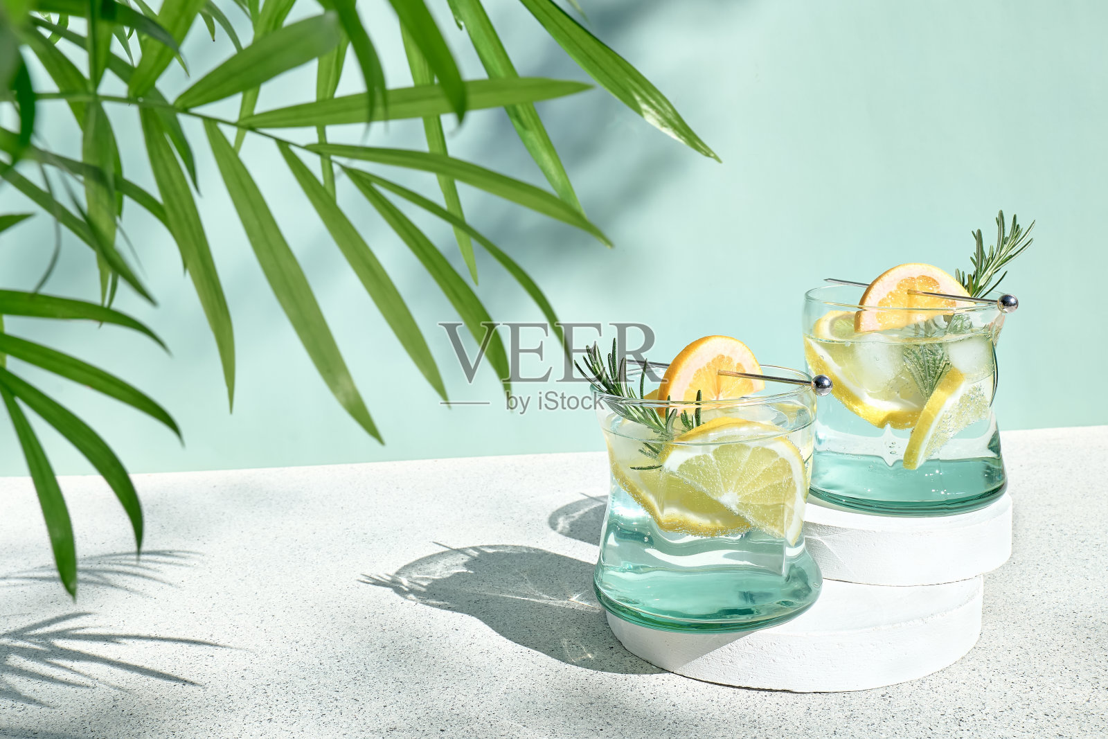 夏季清爽的柠檬水饮料或酒精鸡尾酒，加冰，迷迭香和柠檬片在淡绿色表面。新鲜健康的冷柠檬饮料。和柠檬水。照片摄影图片