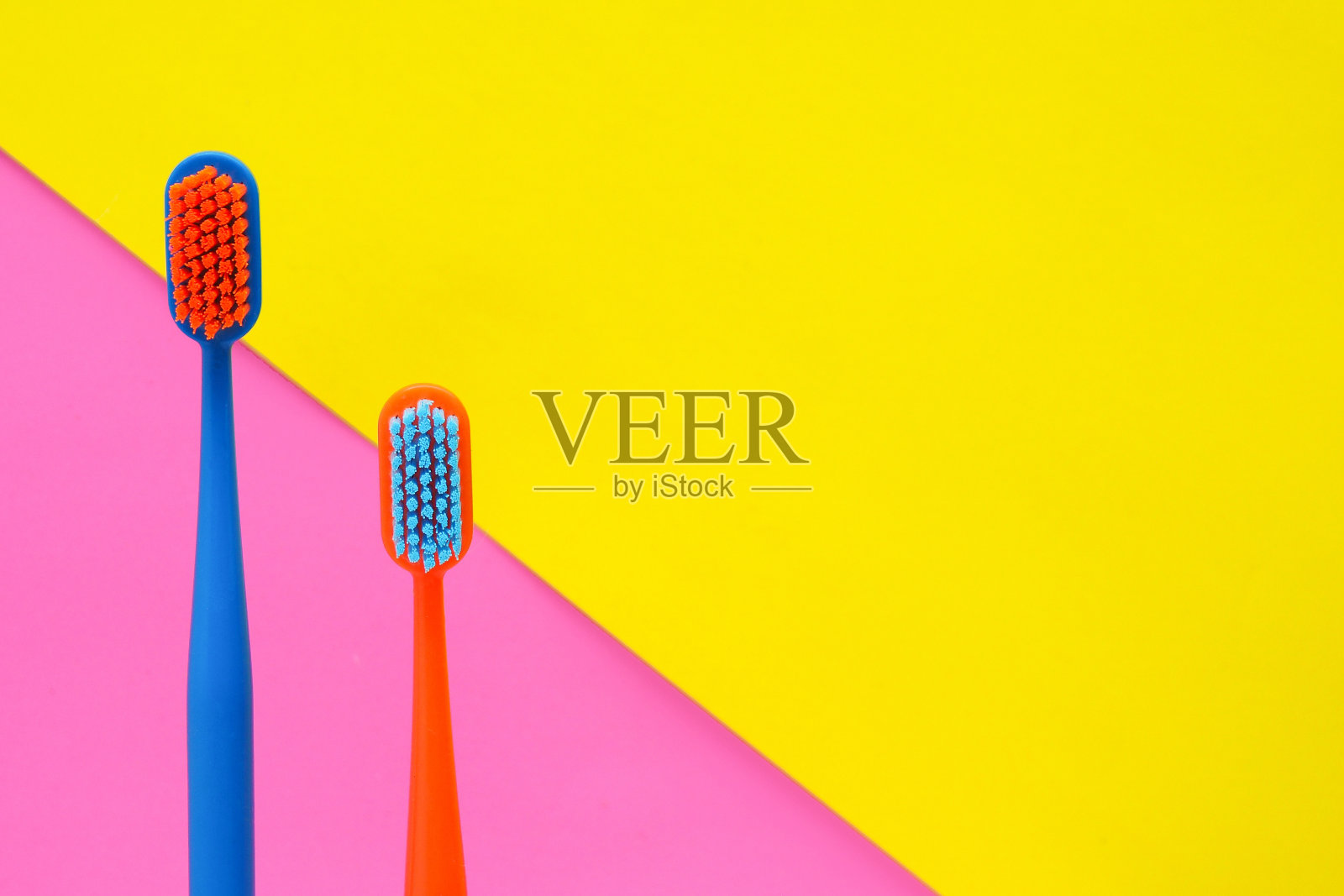 两把多色牙刷，以黄粉色为背景。副本的空间。照片摄影图片