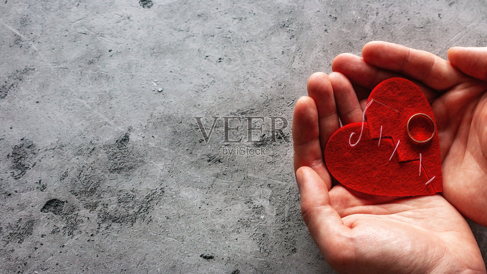 用手捧着一颗用线缝成的破碎的心和一枚结婚戒指，在灰色的背景上写着离婚的概念照片摄影图片