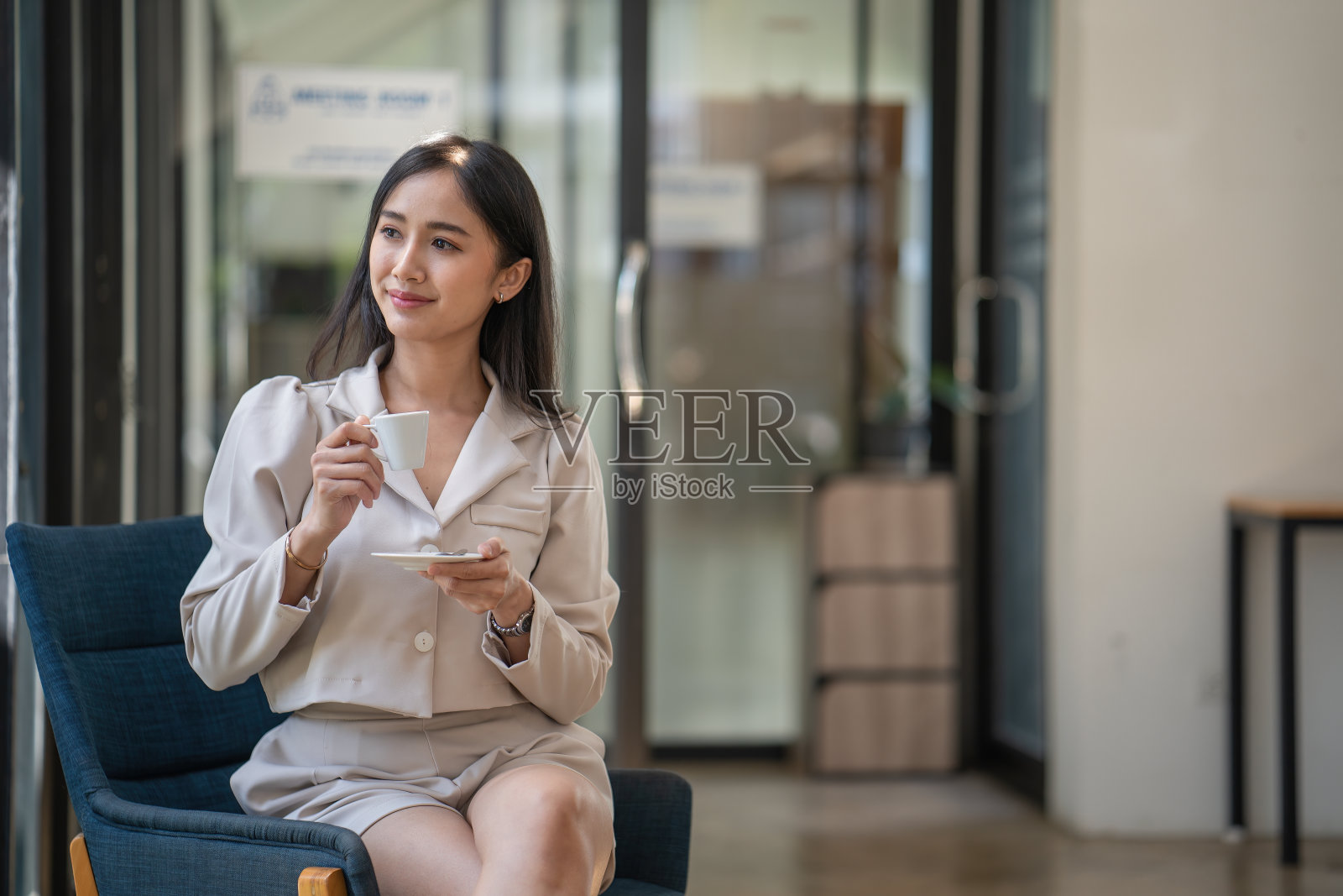 年轻的亚洲职业女性坐在办公室的椅子上喝着咖啡。照片摄影图片