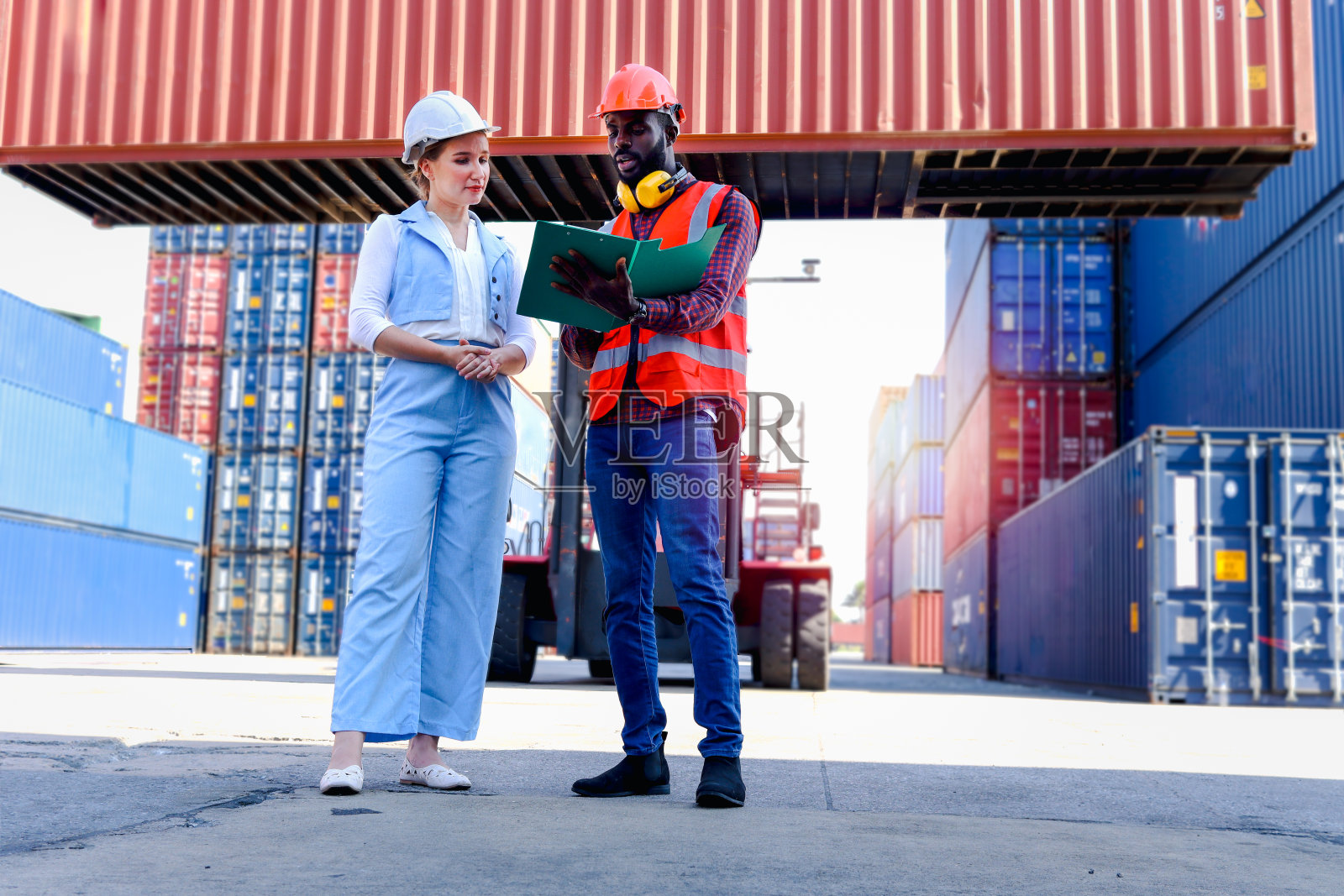 图为，身穿安全背心、头戴安全帽的2名工人正在物流集装箱堆场进行讨论。非裔美国工程师与漂亮的金发女老板在工作场所交谈。照片摄影图片