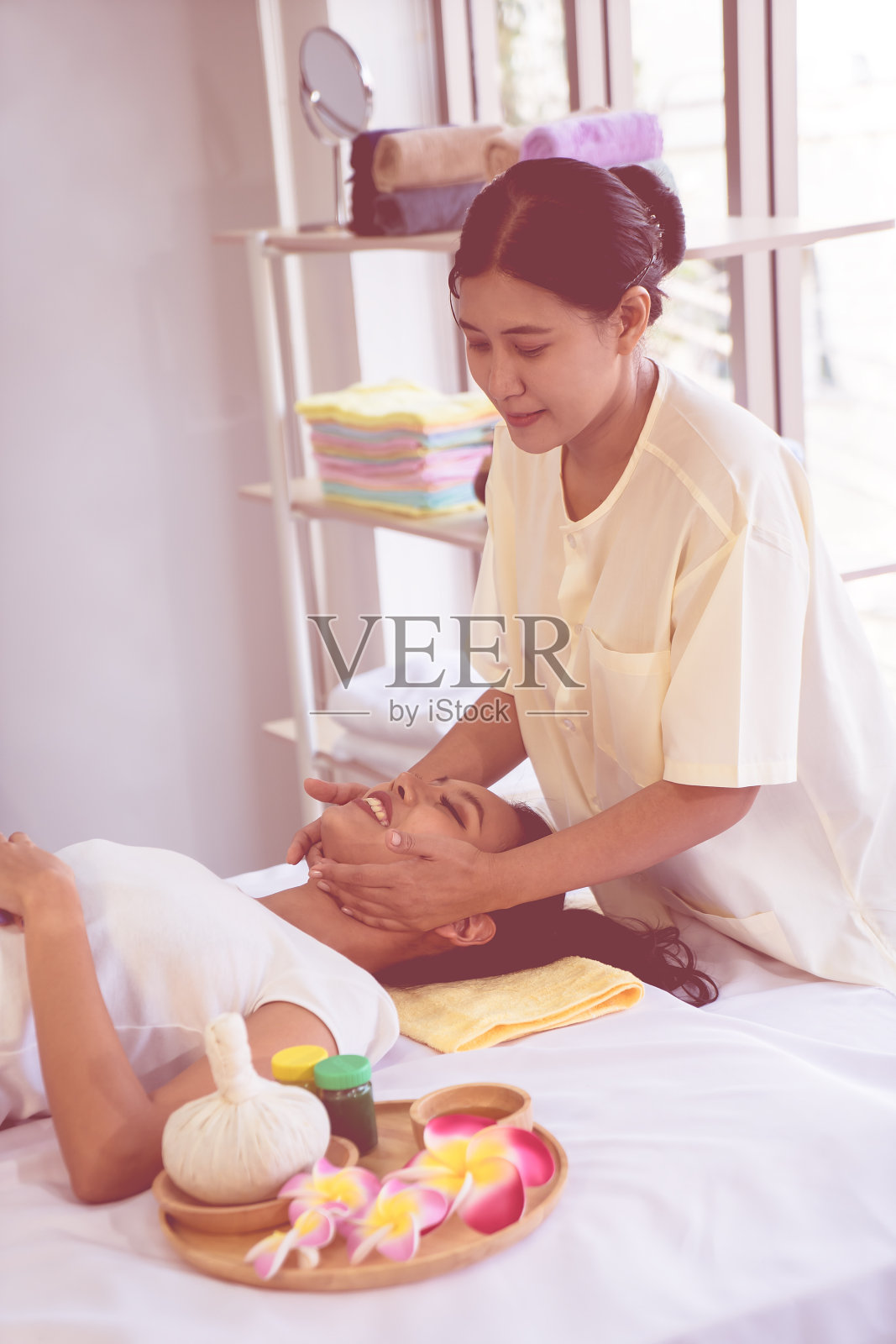 泰国按摩师正在泰国传统水疗中心给一位亚洲妇女进行头部和面部按摩。照片摄影图片
