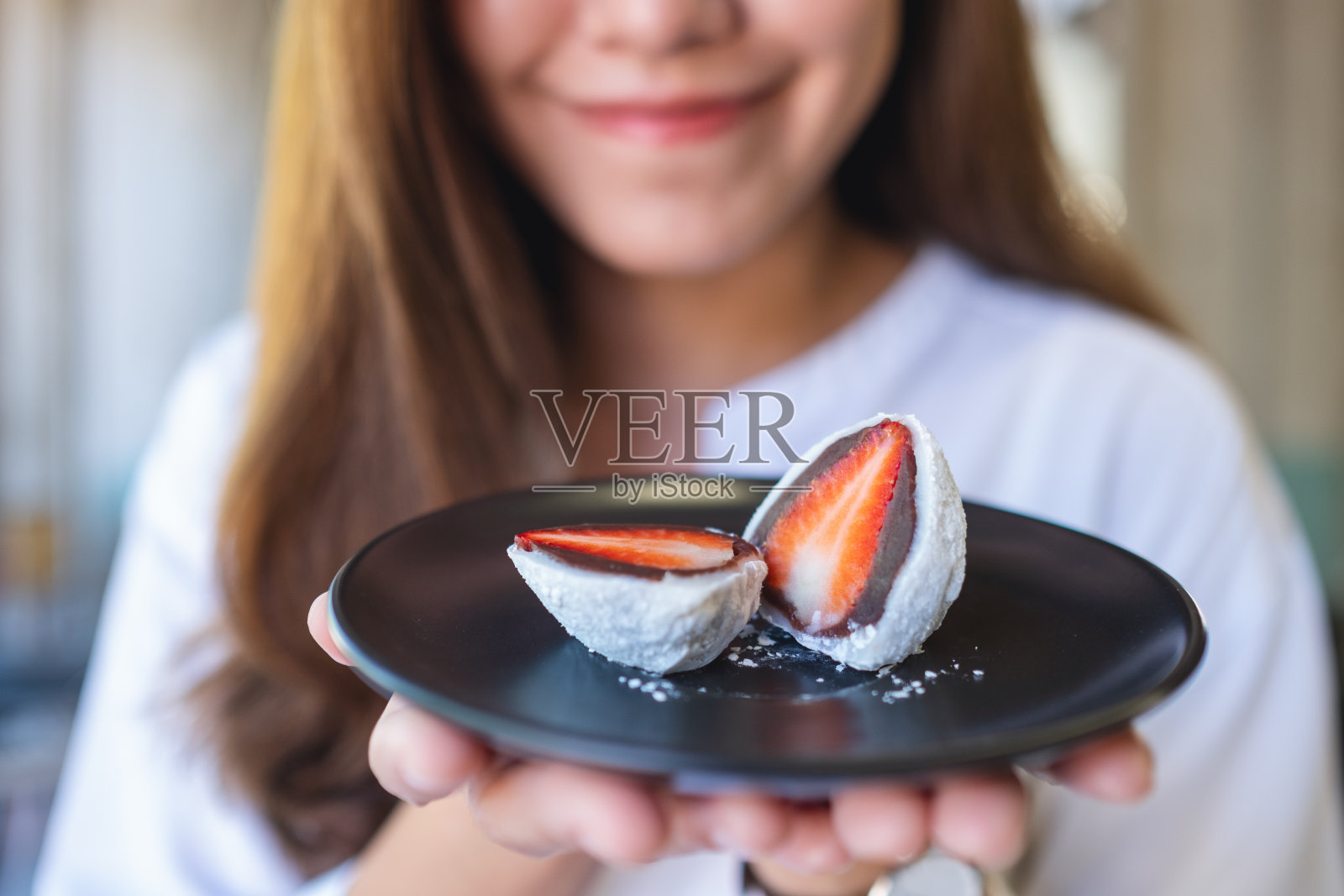 一个年轻女子的特写图像，拿着一盘草莓Mochi或一护大福，甜红豆甜点照片摄影图片
