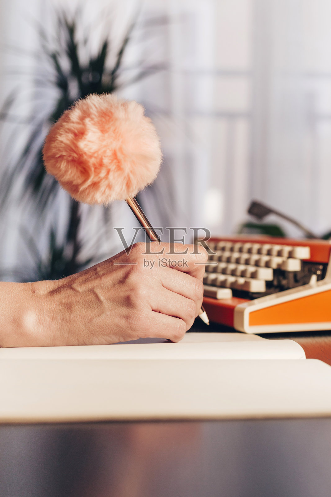 女人的笔迹与粉红色的绒球笔和复古的打字机背景照片摄影图片