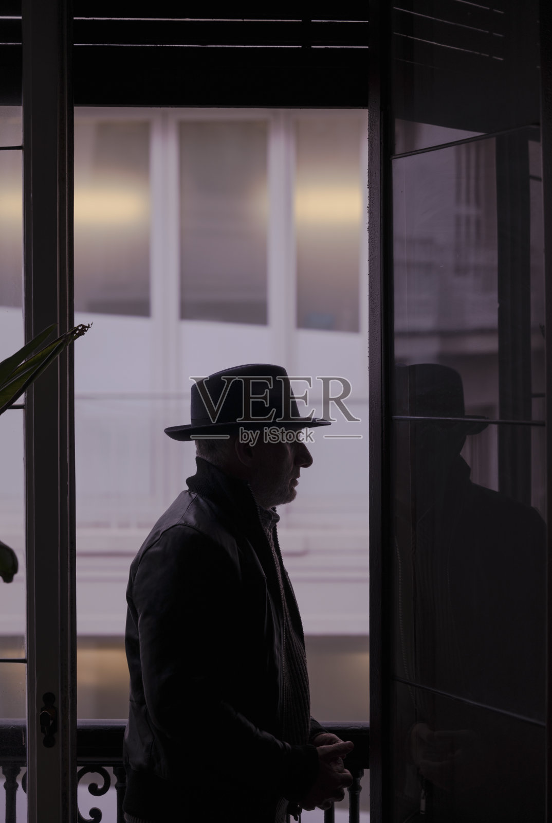 一名戴着帽子、穿着皮夹克的成年男子站在阳台上的肖像。马德里,西班牙照片摄影图片