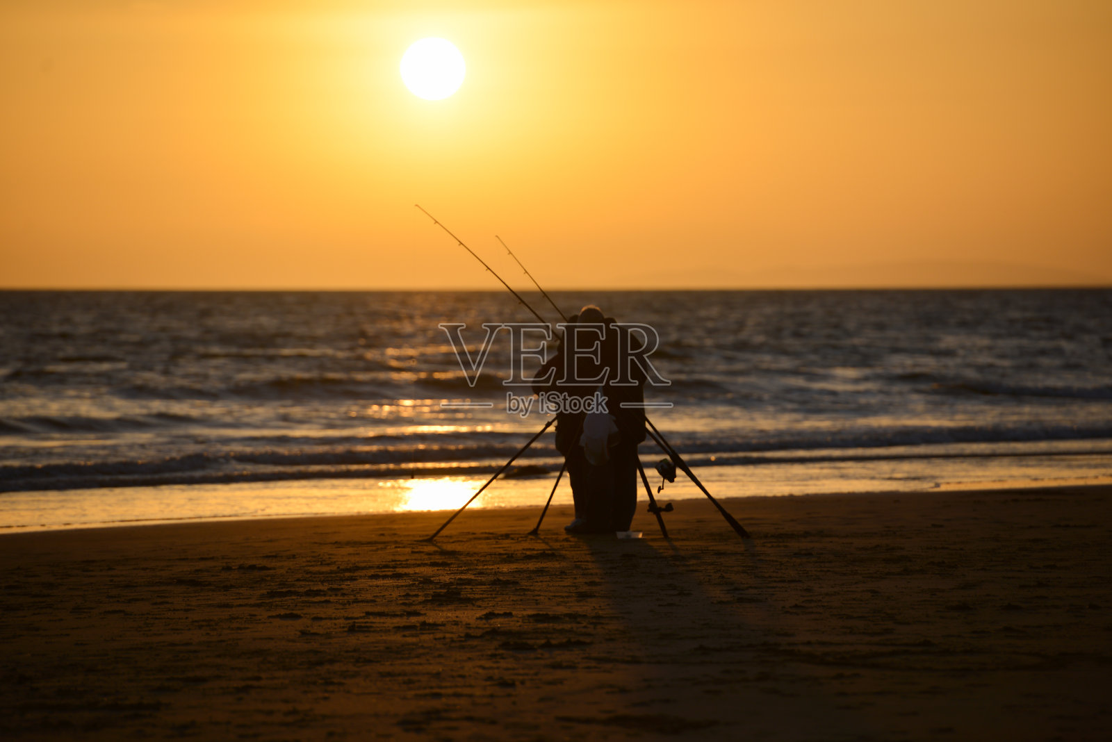夕阳西下，空荡的海滩上的渔夫，夕阳映衬着他和他的钓竿，营造出一种宁静祥和的景象。照片摄影图片