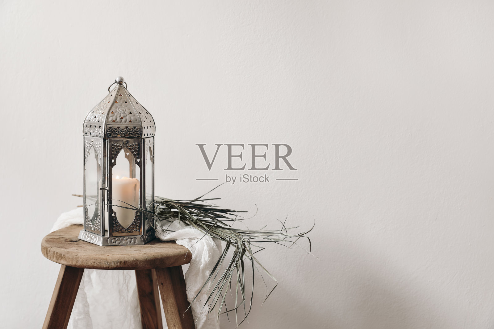 燃烧着银色摩洛哥阿拉伯灯笼。将棕榈叶和棉布放在木凳上晾干。穆斯林节日斋月卡里姆或波西米亚婚礼的贺卡。喜庆的静物背景。照片摄影图片