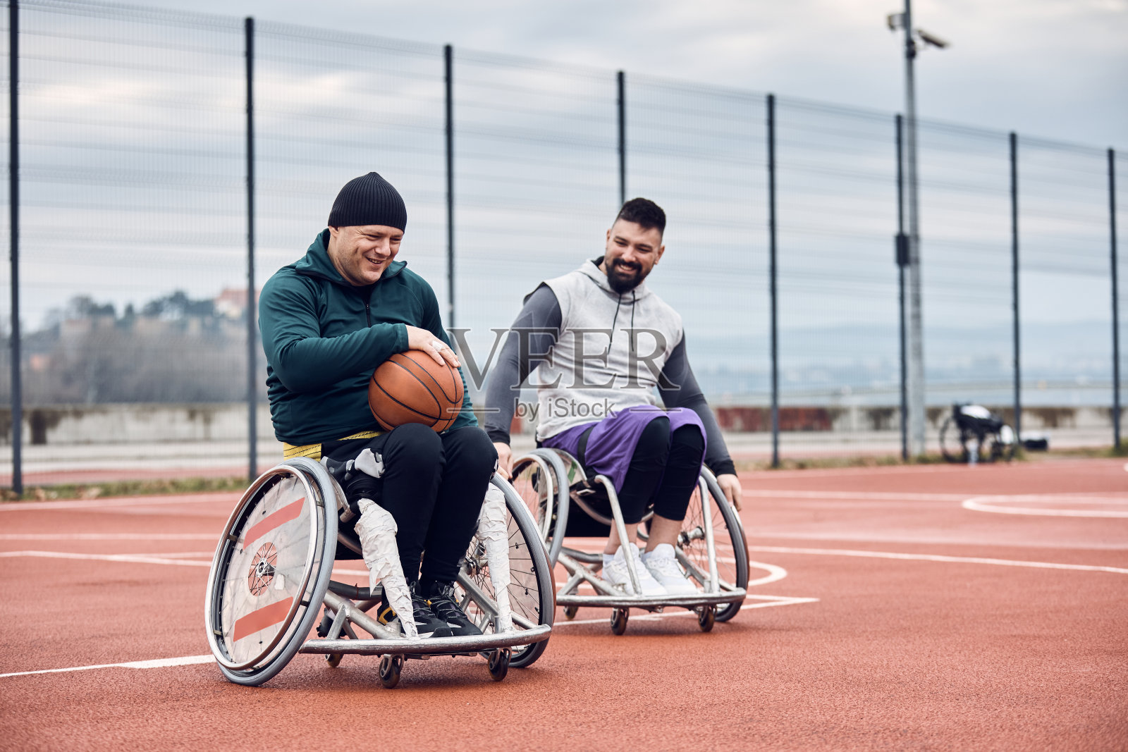 快乐的运动员坐在轮椅上，享受在户外打篮球。照片摄影图片