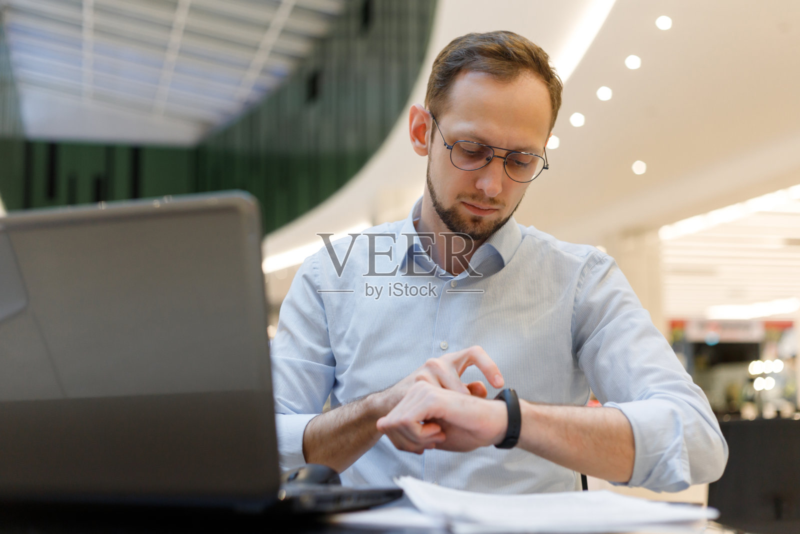 工作时使用智能健身手环。商人坐在桌旁，触摸智能手表照片摄影图片