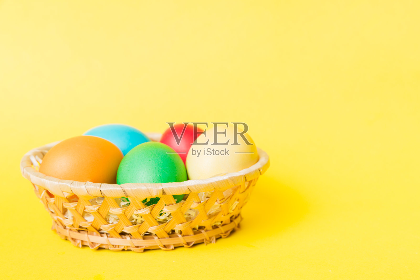 多色复活节彩蛋在彩色背景编织篮。彩色的复活节彩蛋。假日概念与复制空间照片摄影图片