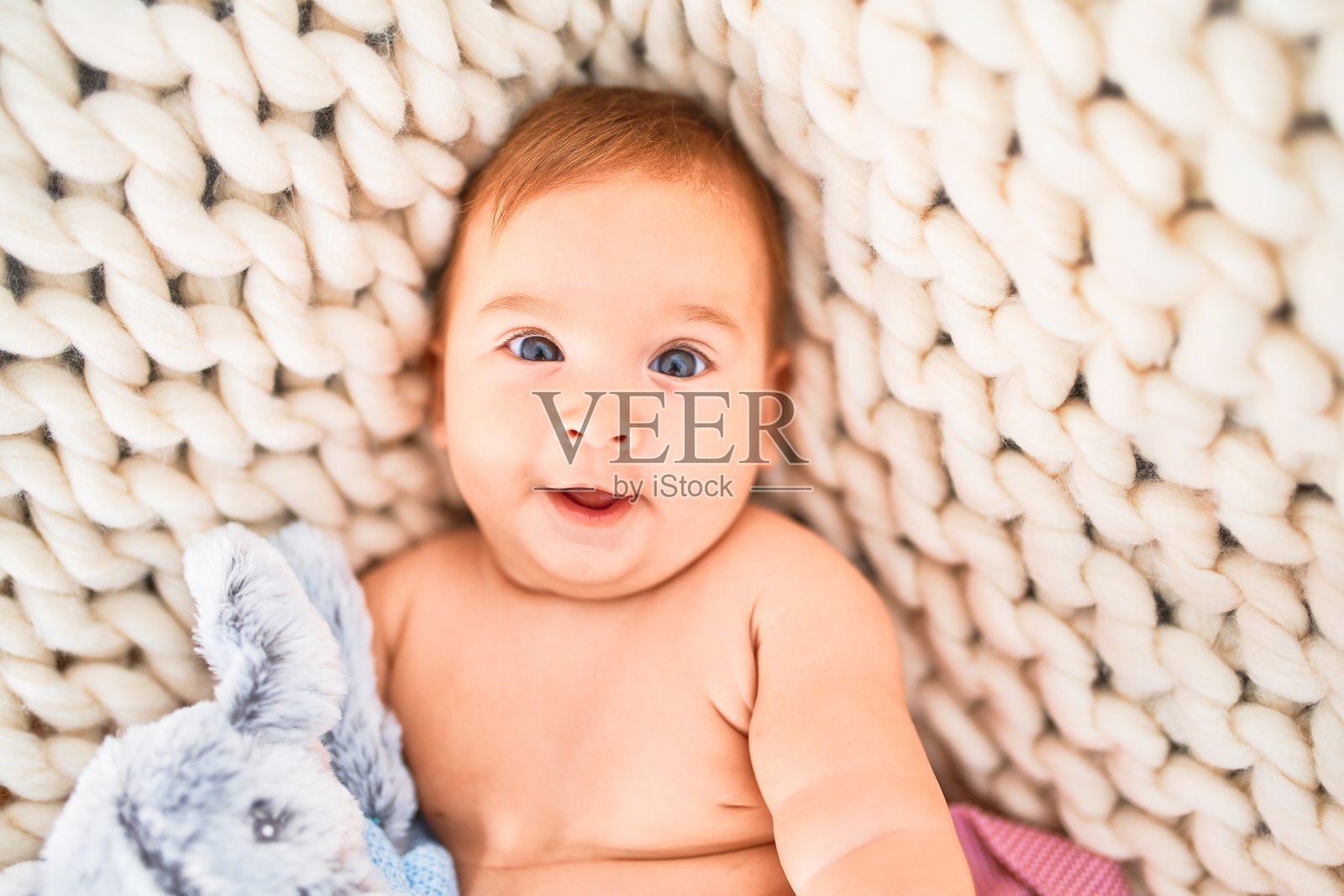 可爱的宝宝躺在沙发上的毯子上开心地笑着回家。新生儿脸上带着微笑，放松和休息的泰迪熊舒适照片摄影图片