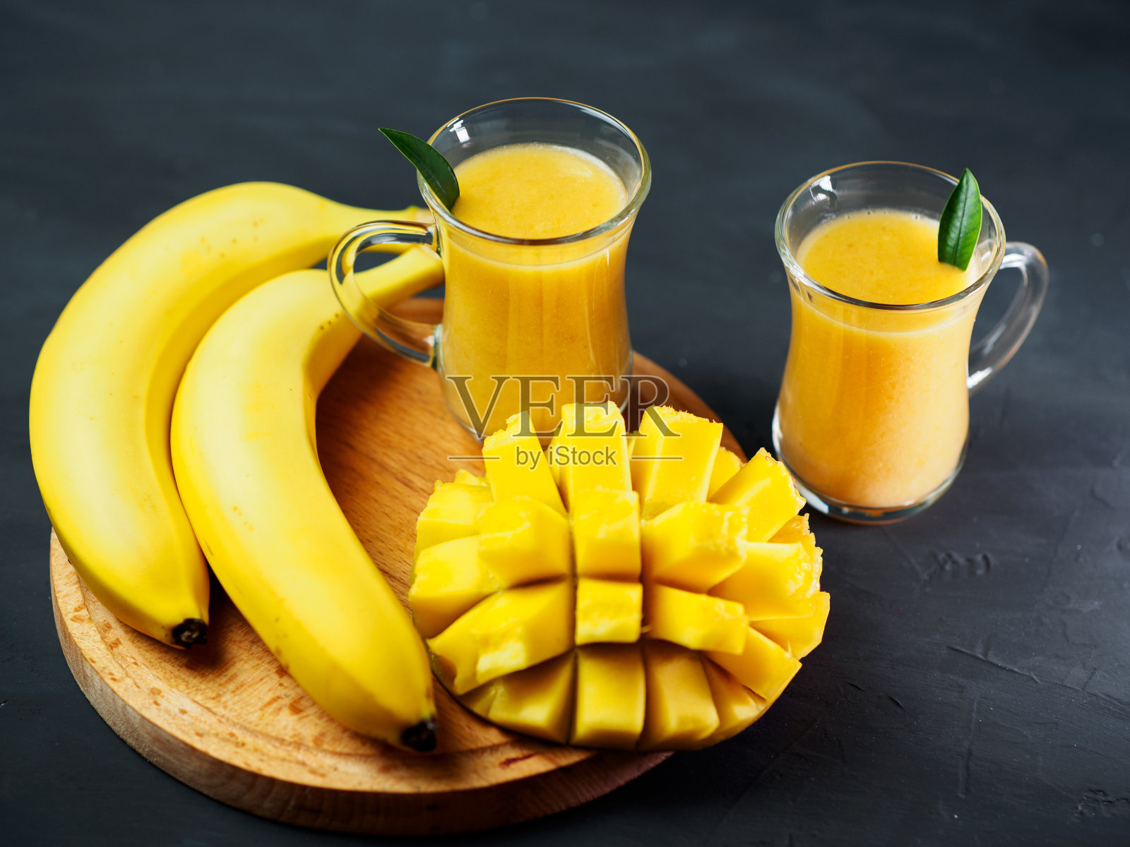 桌上有香蕉和芒果的两杯黄色奶昔照片摄影图片