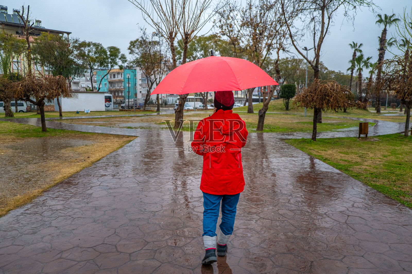 一个女人在雨天打着红伞走在公园里。肖像照片摄影图片