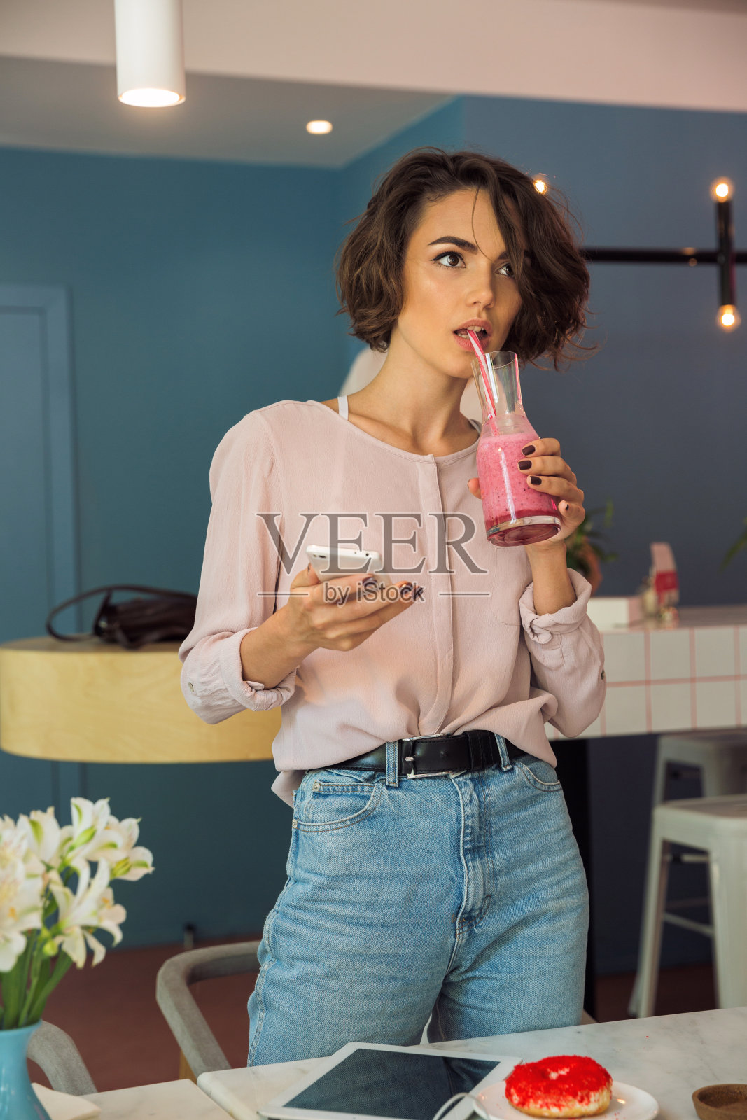 美丽的年轻女孩拿着手机，喝着冰沙照片摄影图片