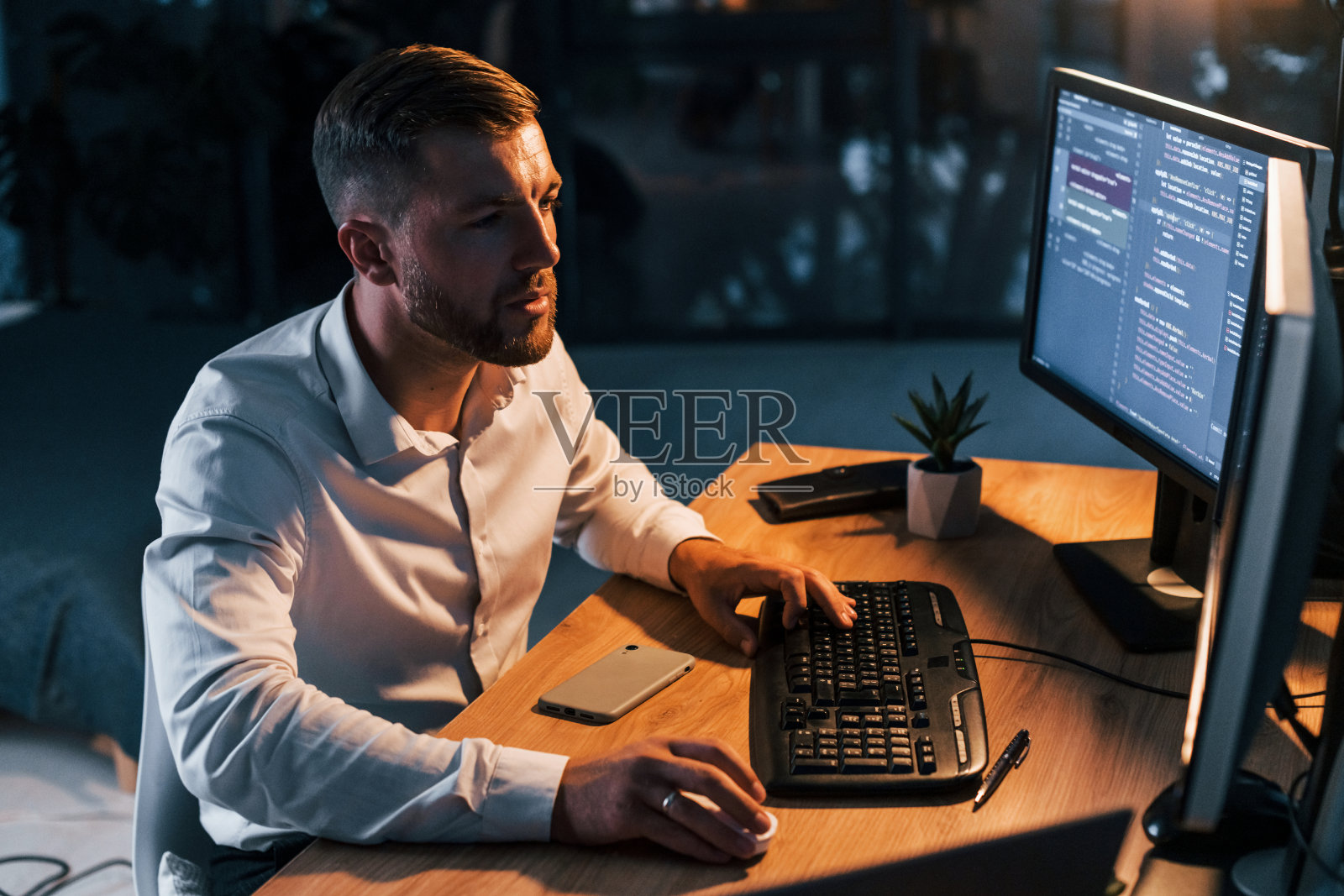 晚上的时间。身着正装的年轻商人坐在有多个屏幕的办公室里照片摄影图片