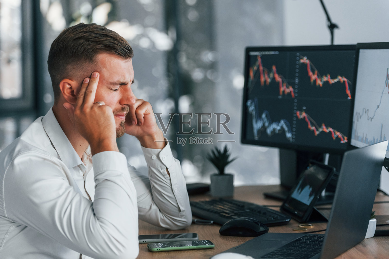 身着正装的年轻商人坐在有多个屏幕的办公室里照片摄影图片