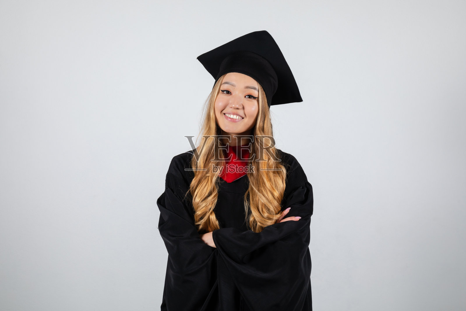 戴着学士帽、身穿学士服、面带微笑的研究生双手交叉照片摄影图片