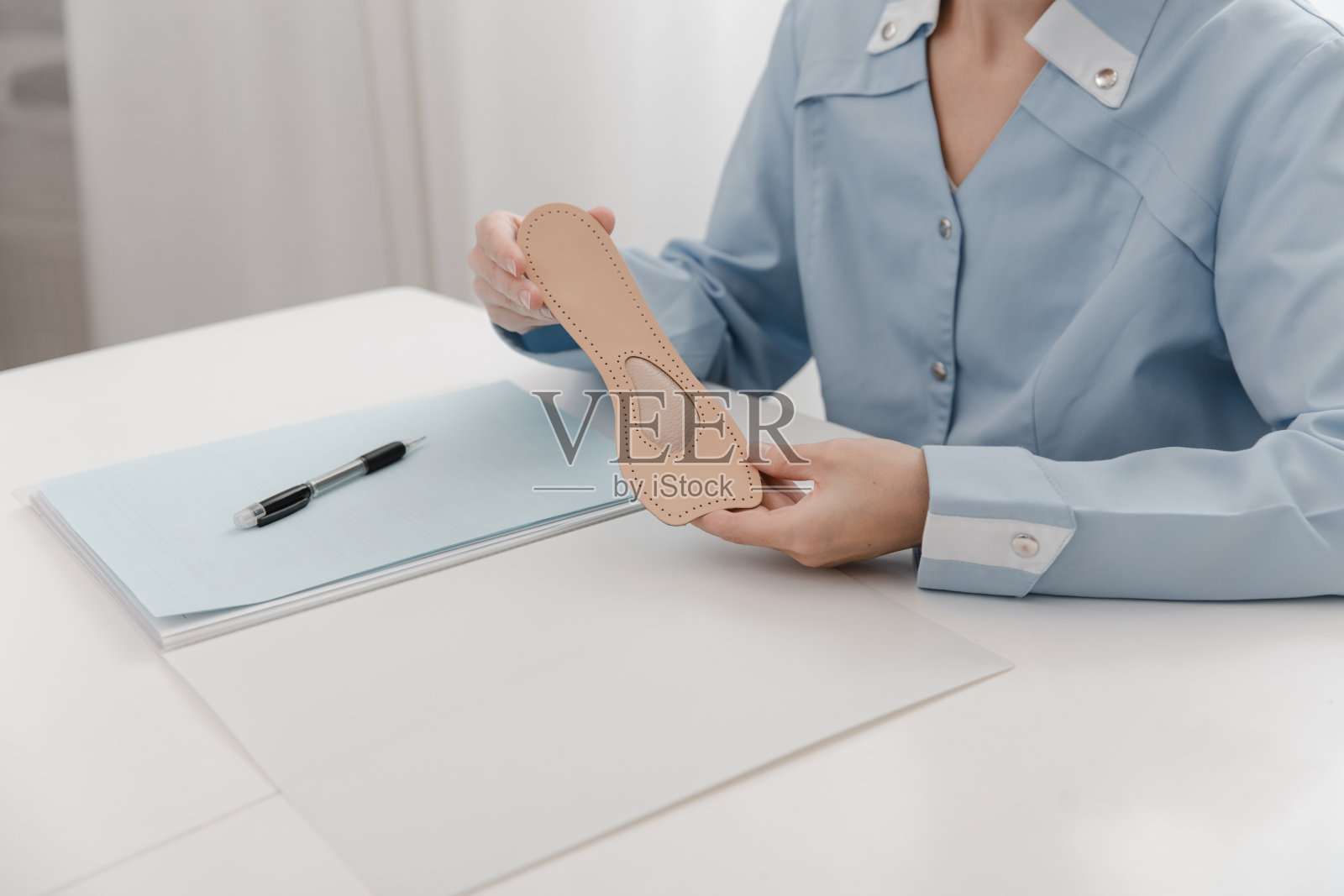 医生坐在桌子旁拿着鞋垫。骨科医生测试医疗设备。矫形鞋垫。足部护理。扁平足的修正。治疗和预防扁平足和足部疾病照片摄影图片