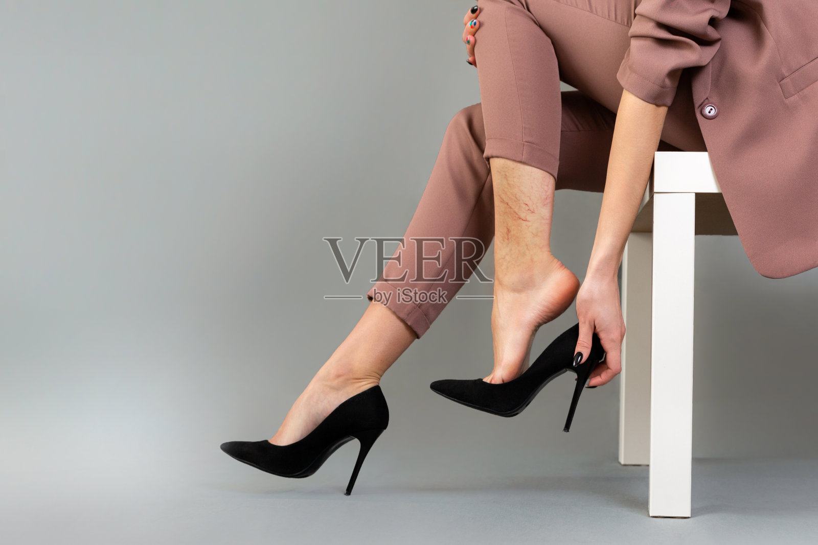 静脉曲张病的概念。一个穿西装的女人脱下了高跟鞋。腿部可见血管星号。腿关闭。灰色背景照片摄影图片