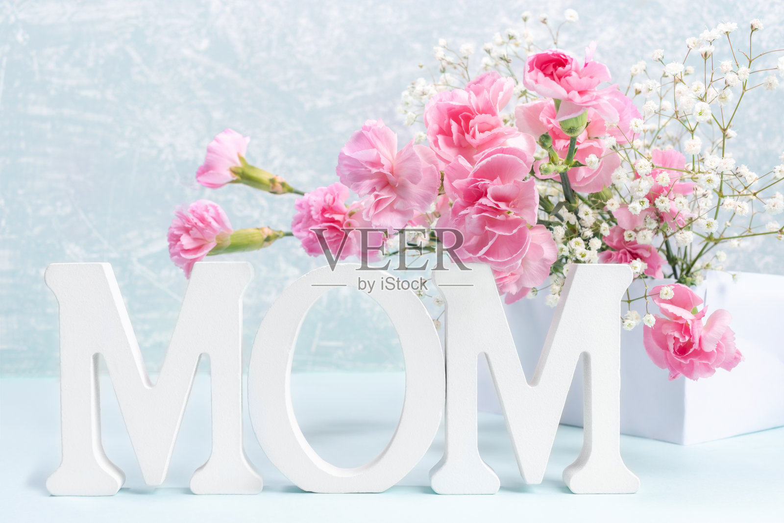 母亲节贺卡上有白色的字母MOM，粉红色的康乃馨和浅灰色的gypsophila花。照片摄影图片