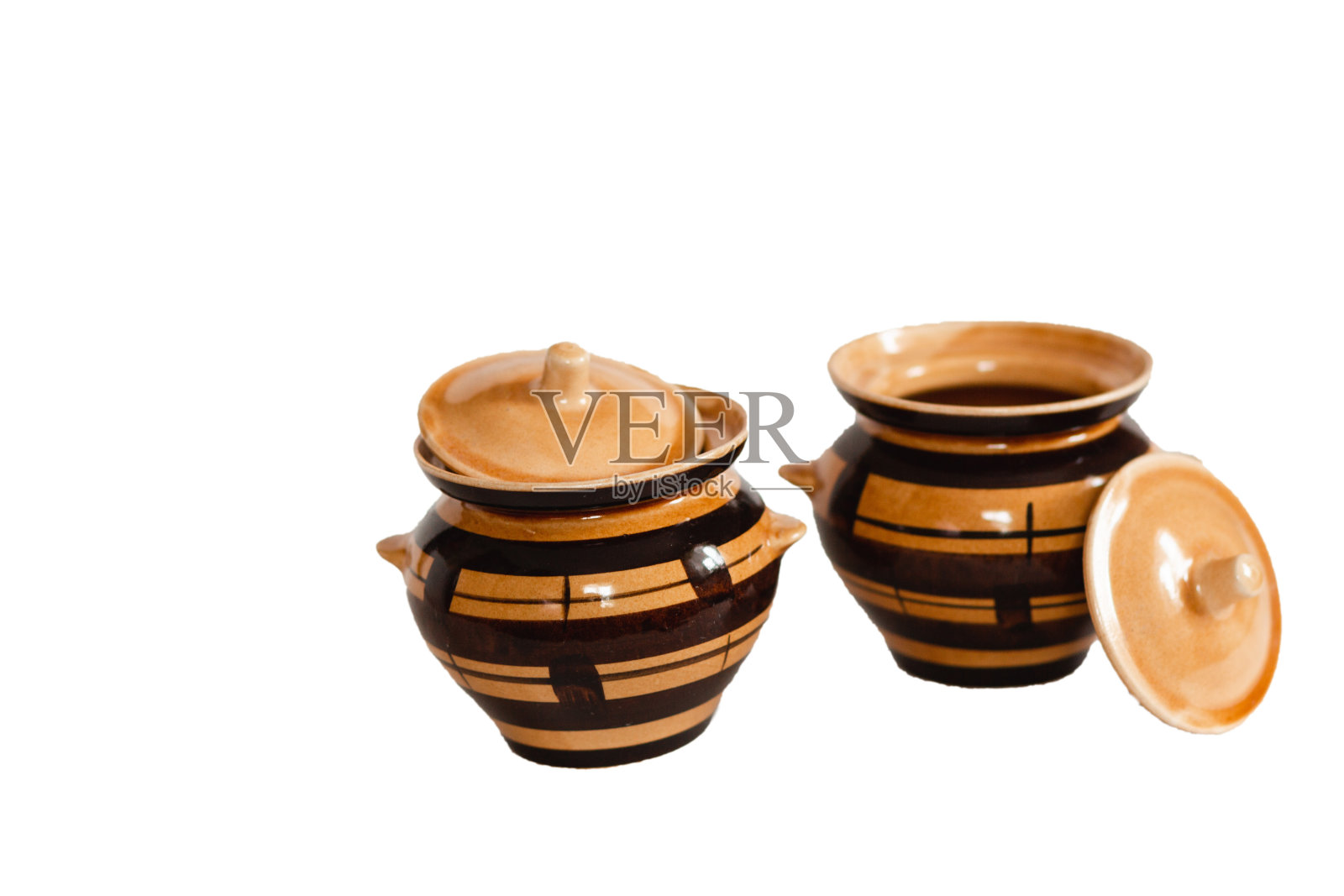 两个闪亮的橙色和黑色的陶罐，上面有一个盖子，微微倾斜在一边，一个在锅的前面。孤立在白色的背景上照片摄影图片