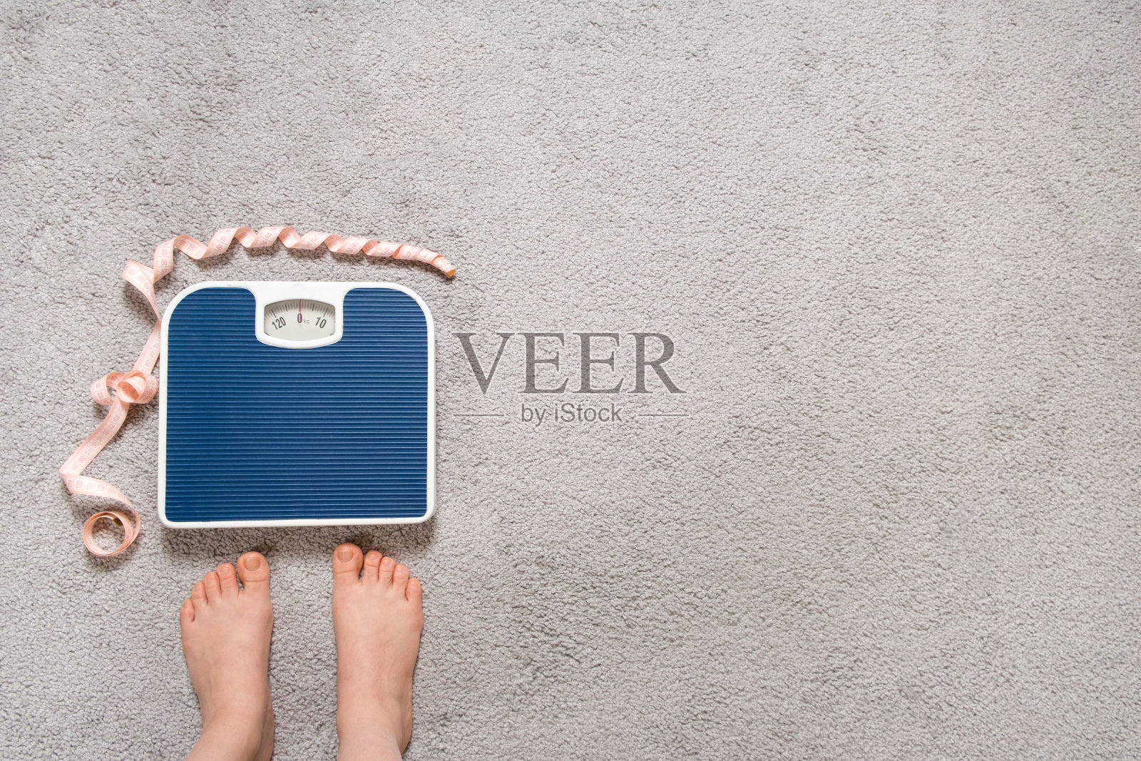 光着脚，地板上的蓝色磅秤上有一根厘米长的卷尺，这是减肥的概念，放文字的地方，俯视图。照片摄影图片