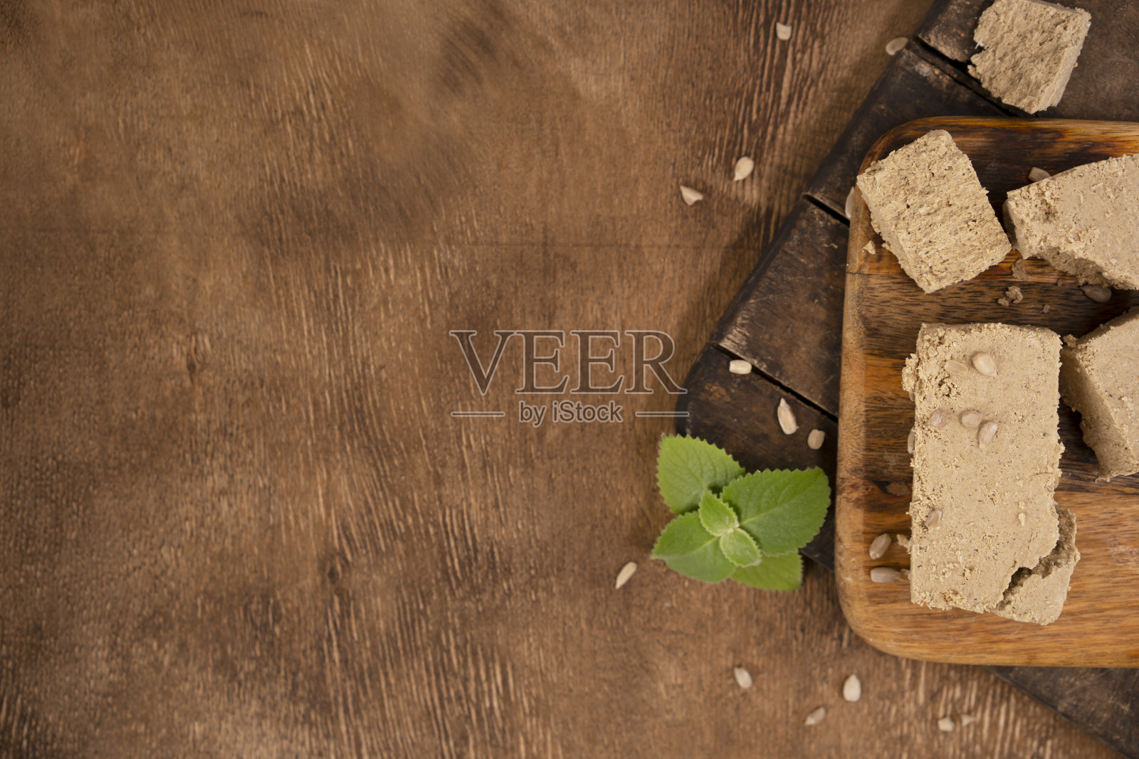 传统的东方甜点哈瓦，葵花籽和薄荷叶放在砧板上。木制背景。前视图。本空间照片摄影图片