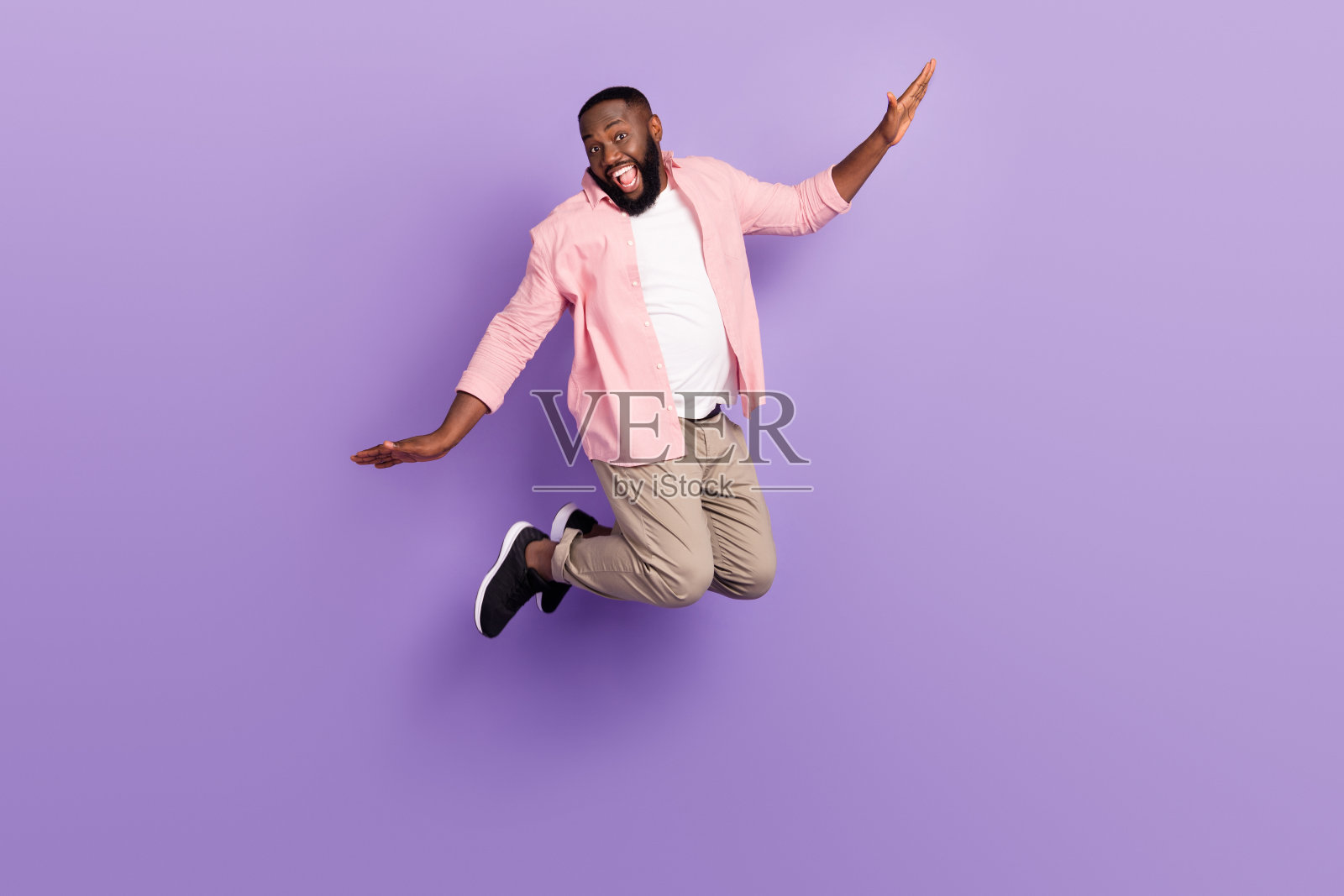 全长照片万岁年轻的家伙跳穿衬衫裤子运动鞋孤立在紫罗兰色的背景照片摄影图片