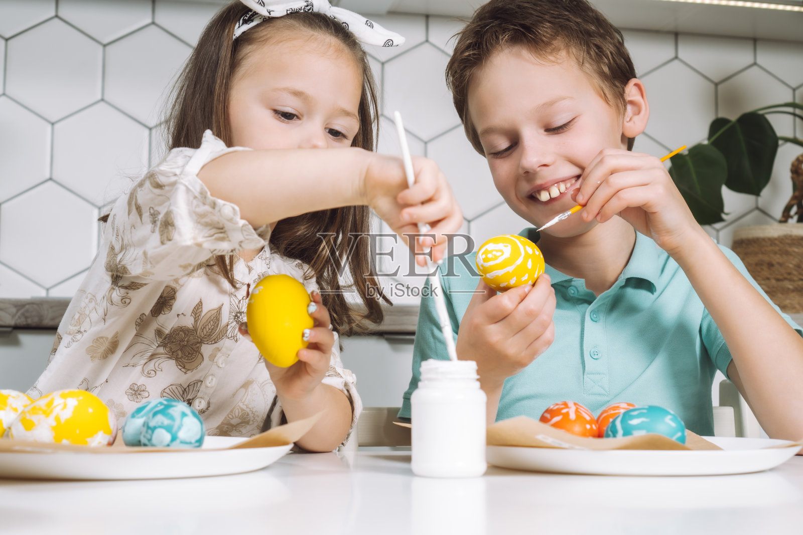 微笑着快乐的两个孩子的肖像小女孩，男孩，绘画，复活节彩蛋，厨房桌子上的画笔。照片摄影图片
