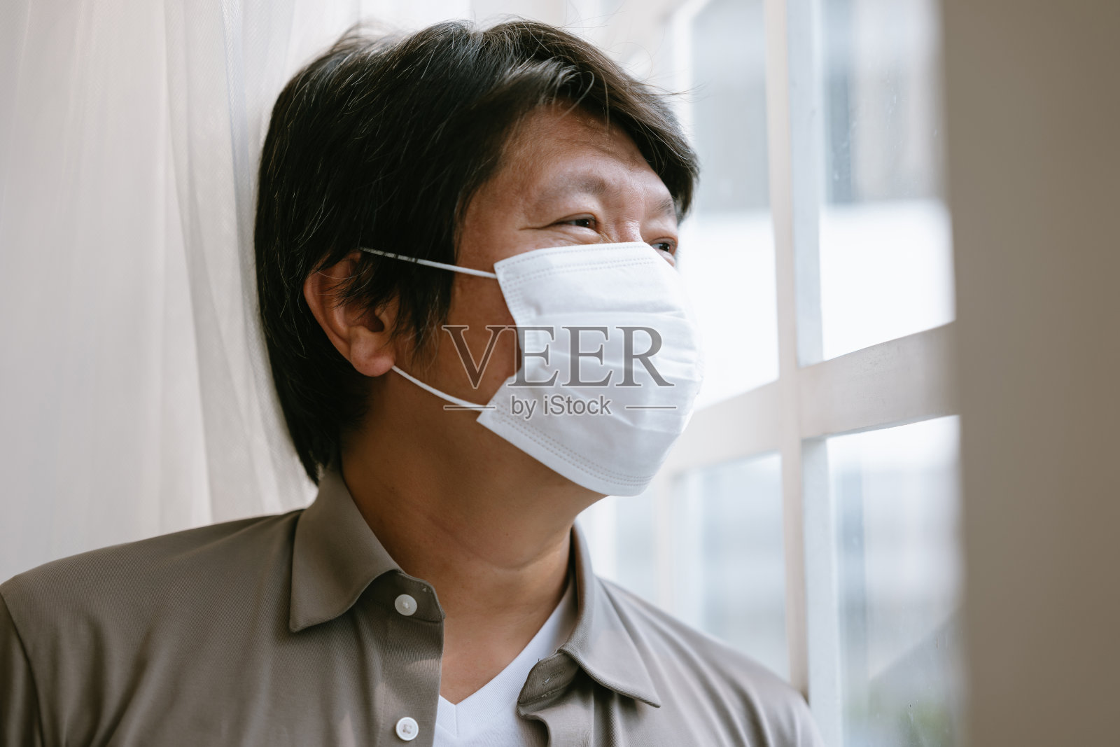 戴口罩的韩国男人在窗边隔离，疫情期间的孤独感照片摄影图片